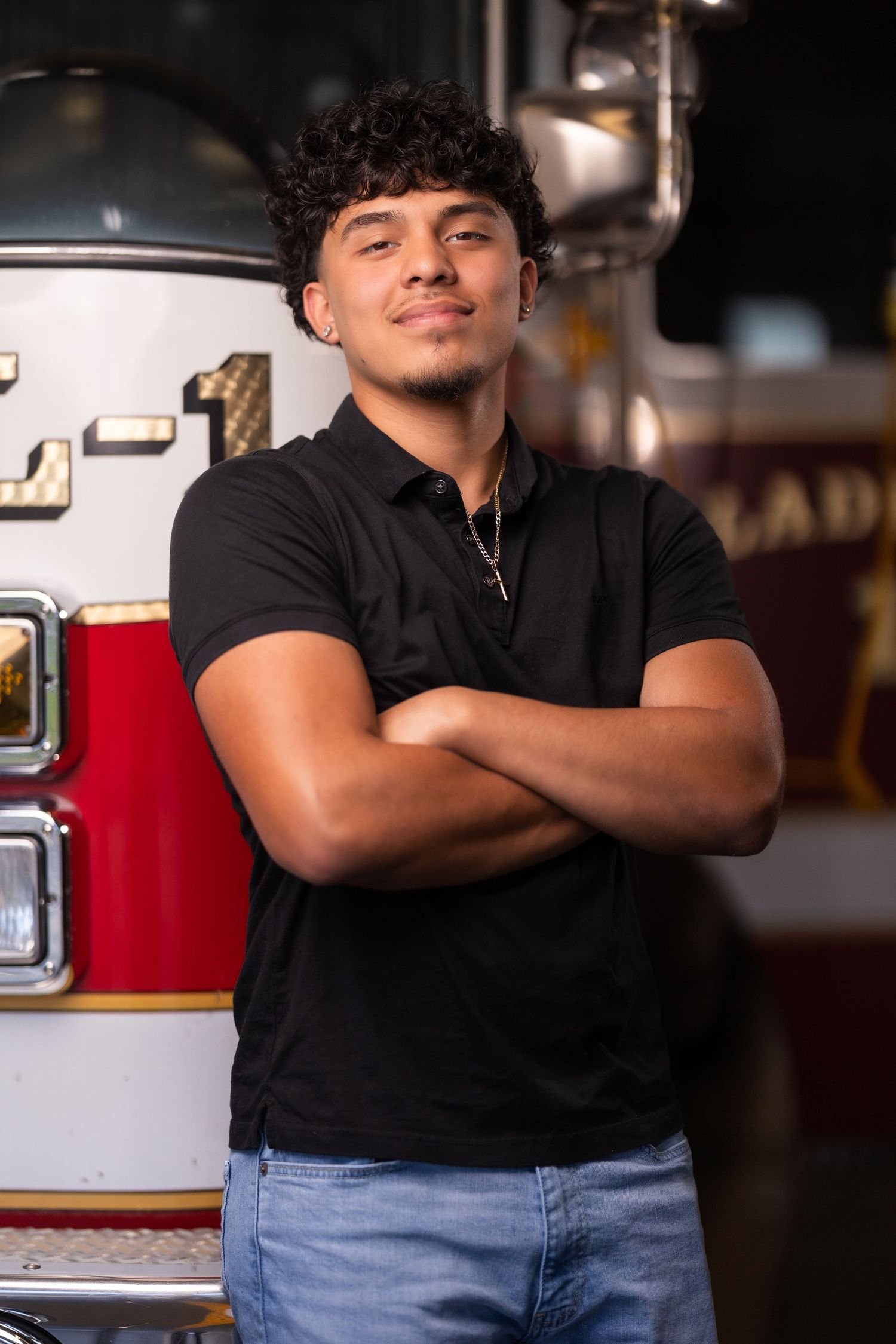 Person in black polo shirt poses with arms crossed in front of a fire truck.