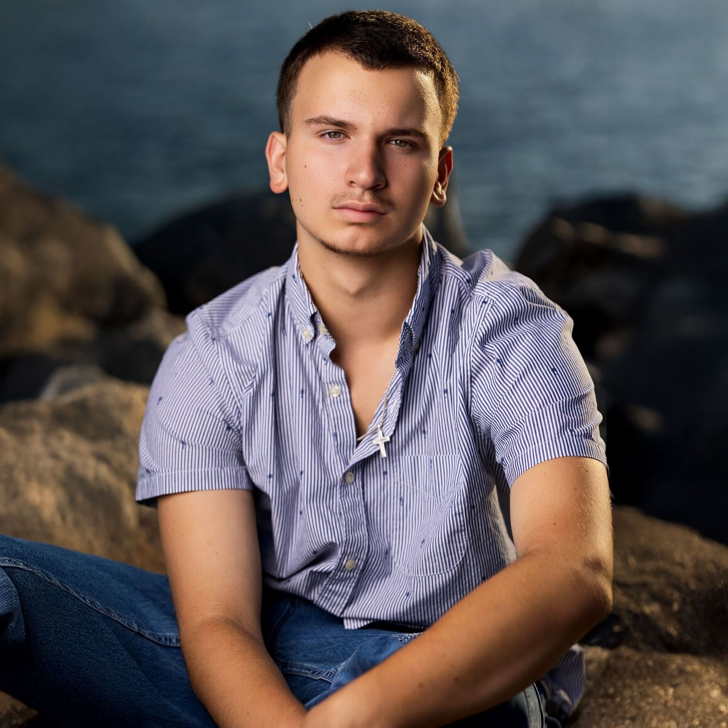 Casual outdoor portrait series on rocky beach wearing light blue shirt.