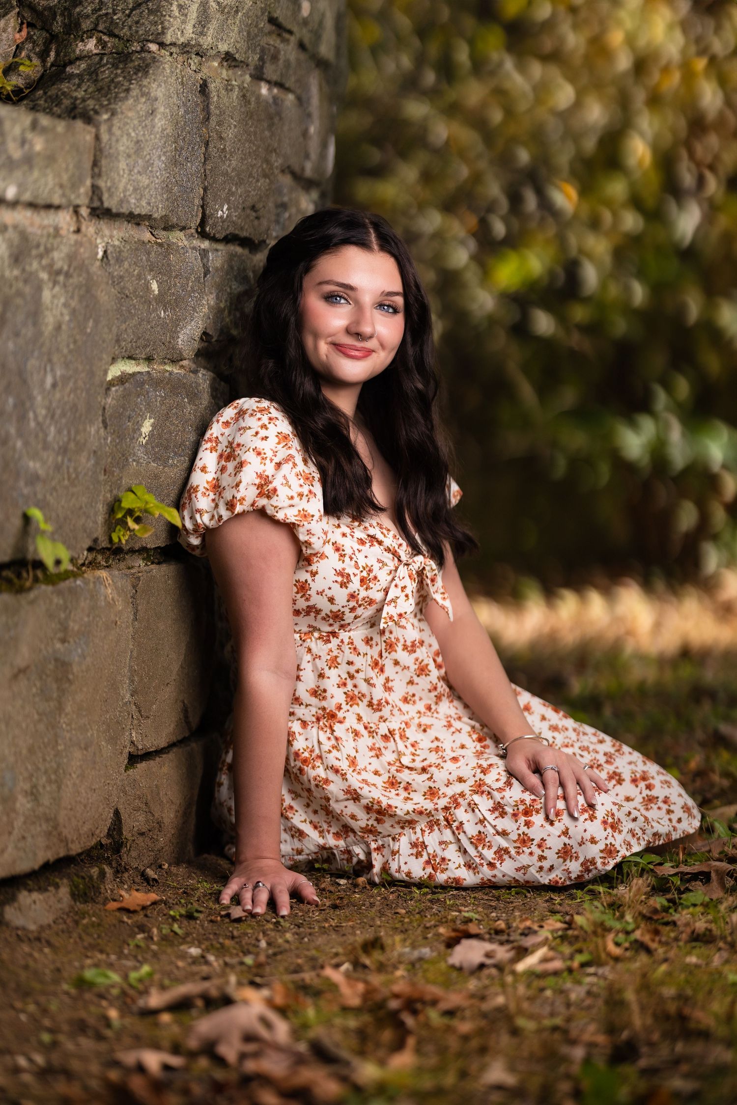 Person in floral dress poses against stone wall in natural setting.