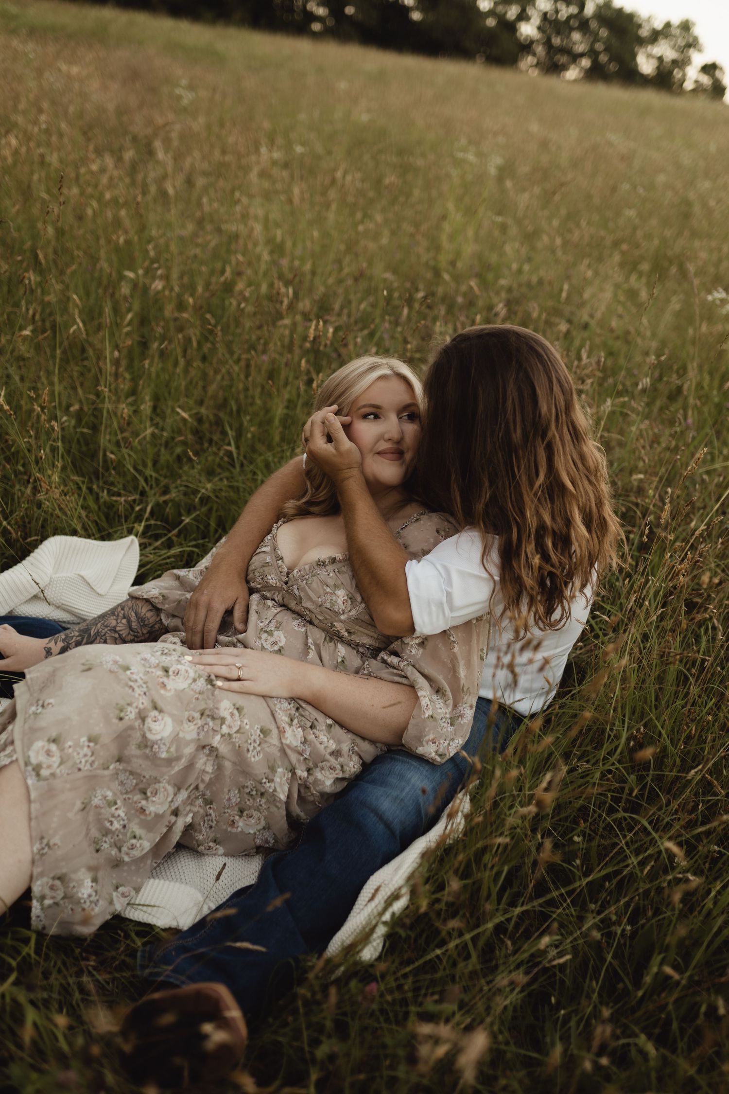 Couple sitting in a lush green field, sharing a tender romantic moment on a blanket at golden hour.