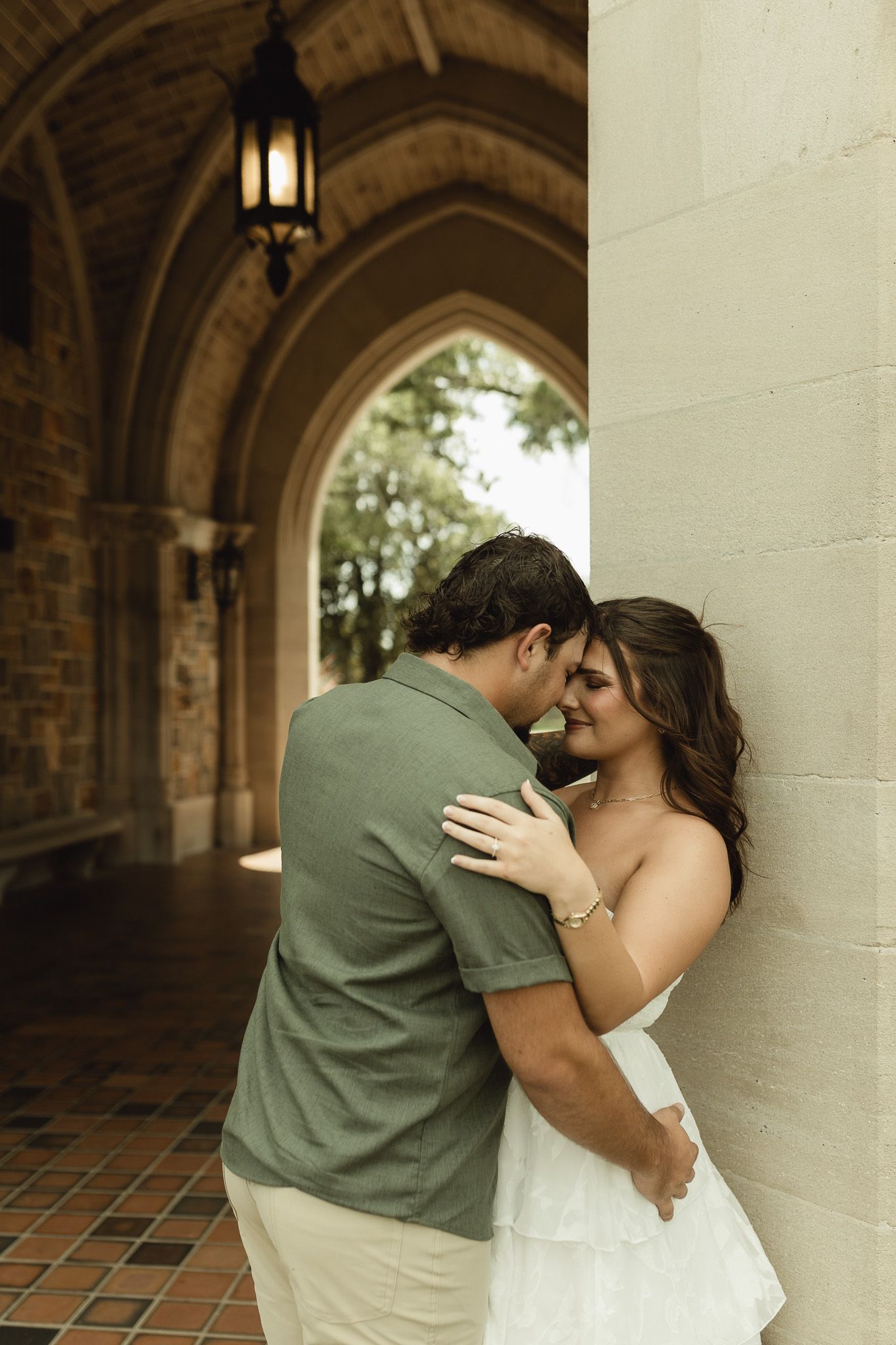 Couple sharing a romantic moment leaning against a stone column under Gothic arched walkway with vintage lantern.
