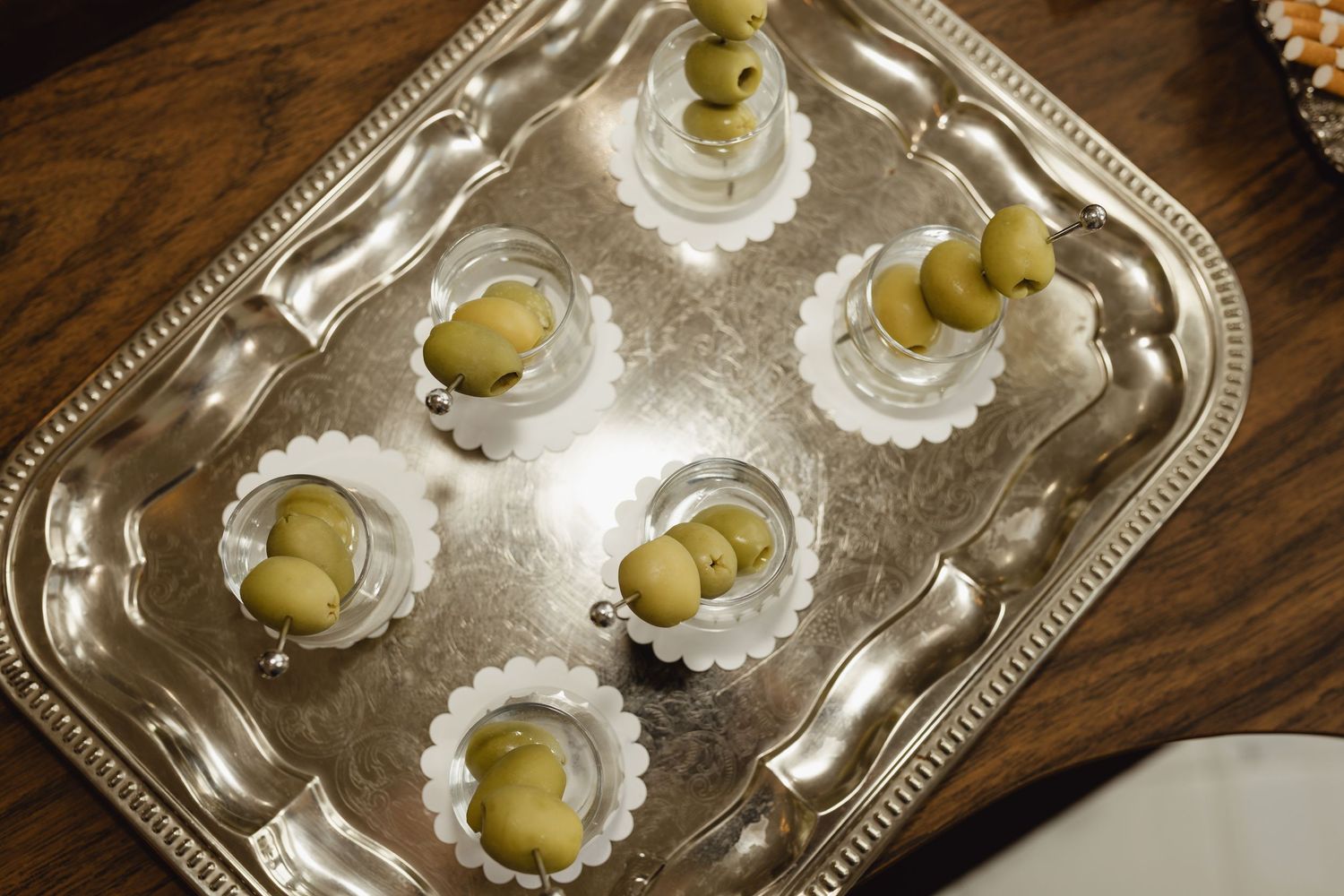 Silver tray with small glasses filled with green olives on toothpicks, elegantly arranged for a party appetizer display.