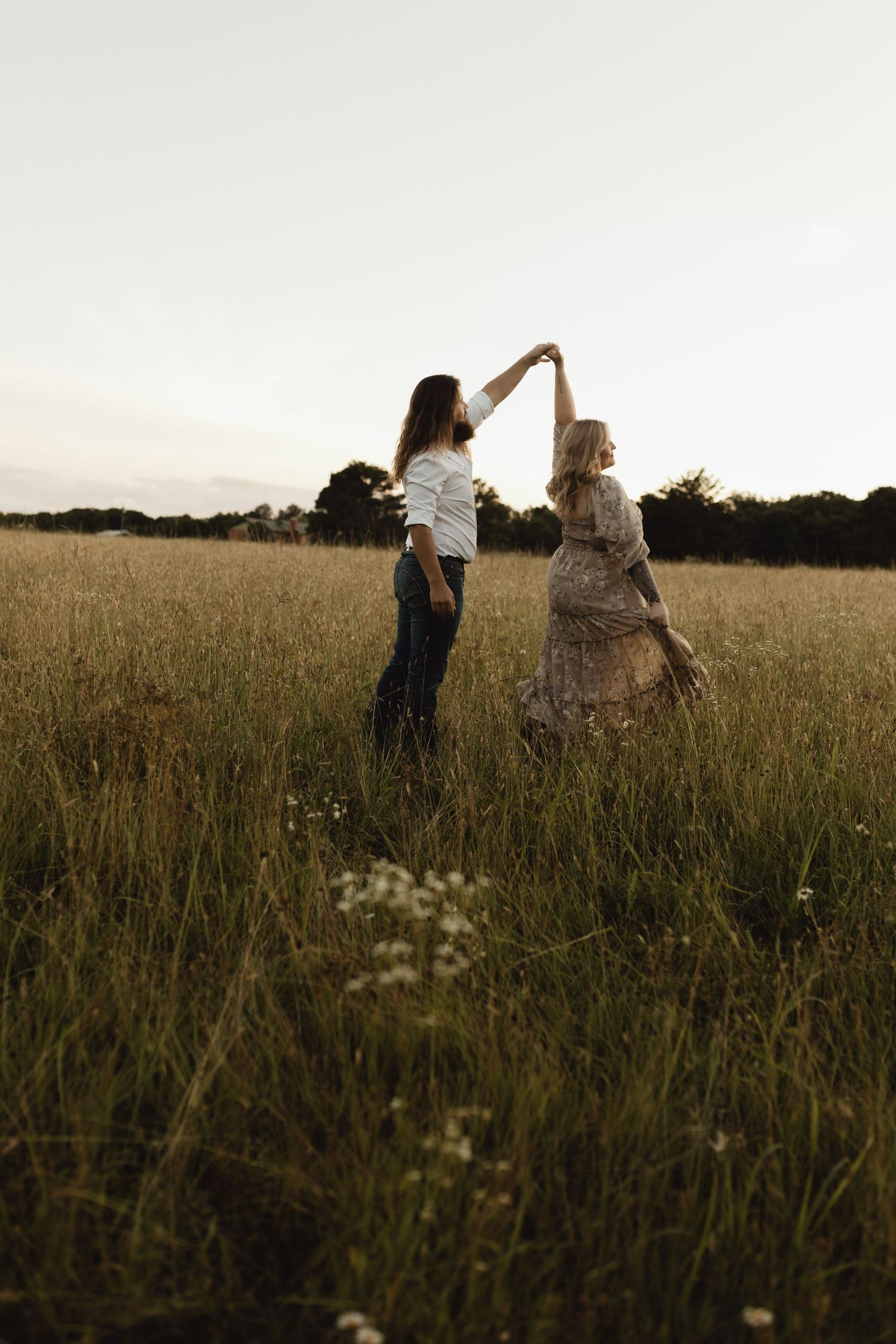 Two women dancing together in a golden field at sunset, one wearing a floral dress, sharing a joyful moment.