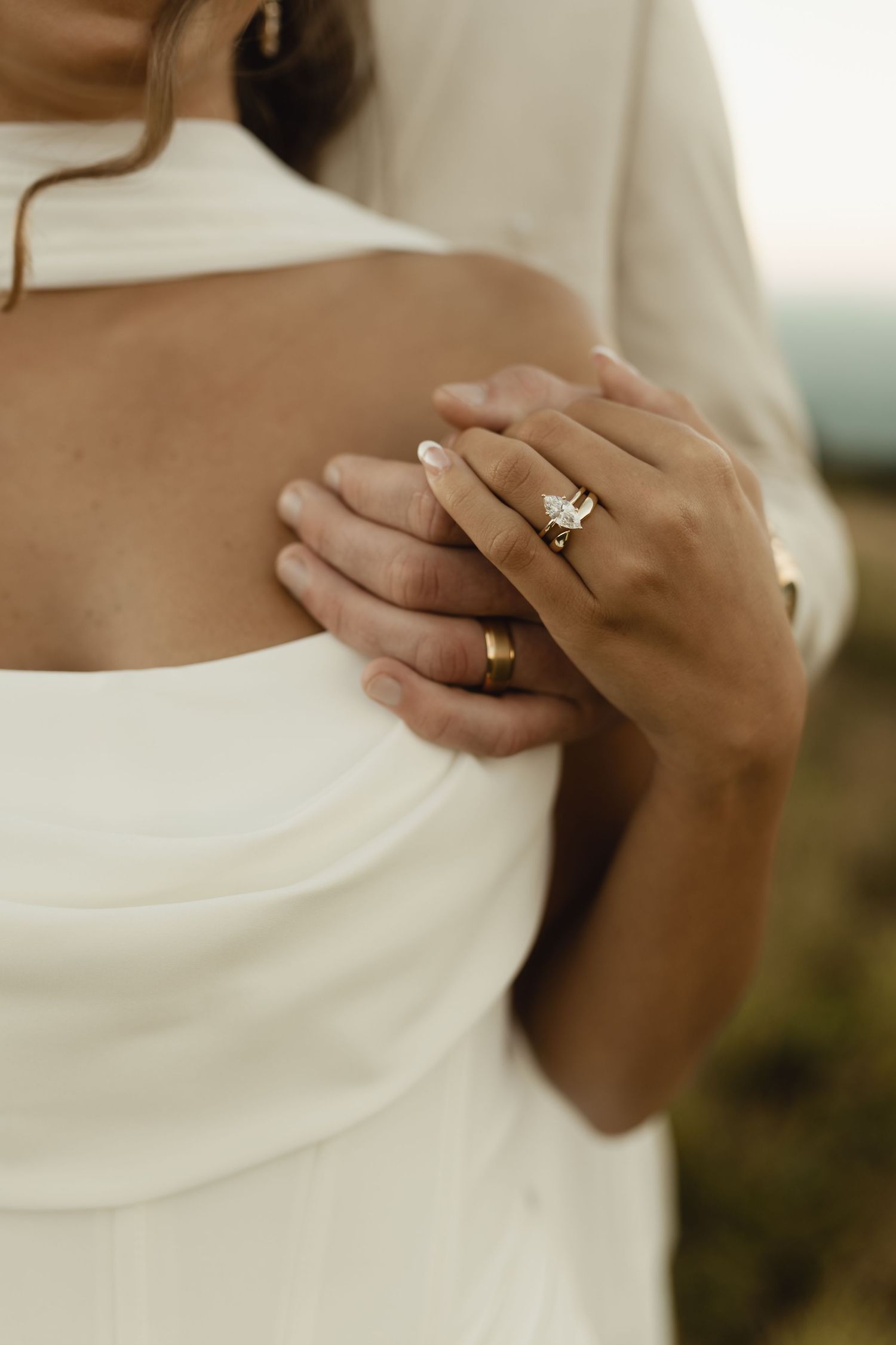 Close-up of bride and groom hands embracing, showcasing diamond engagement ring and gold wedding band.