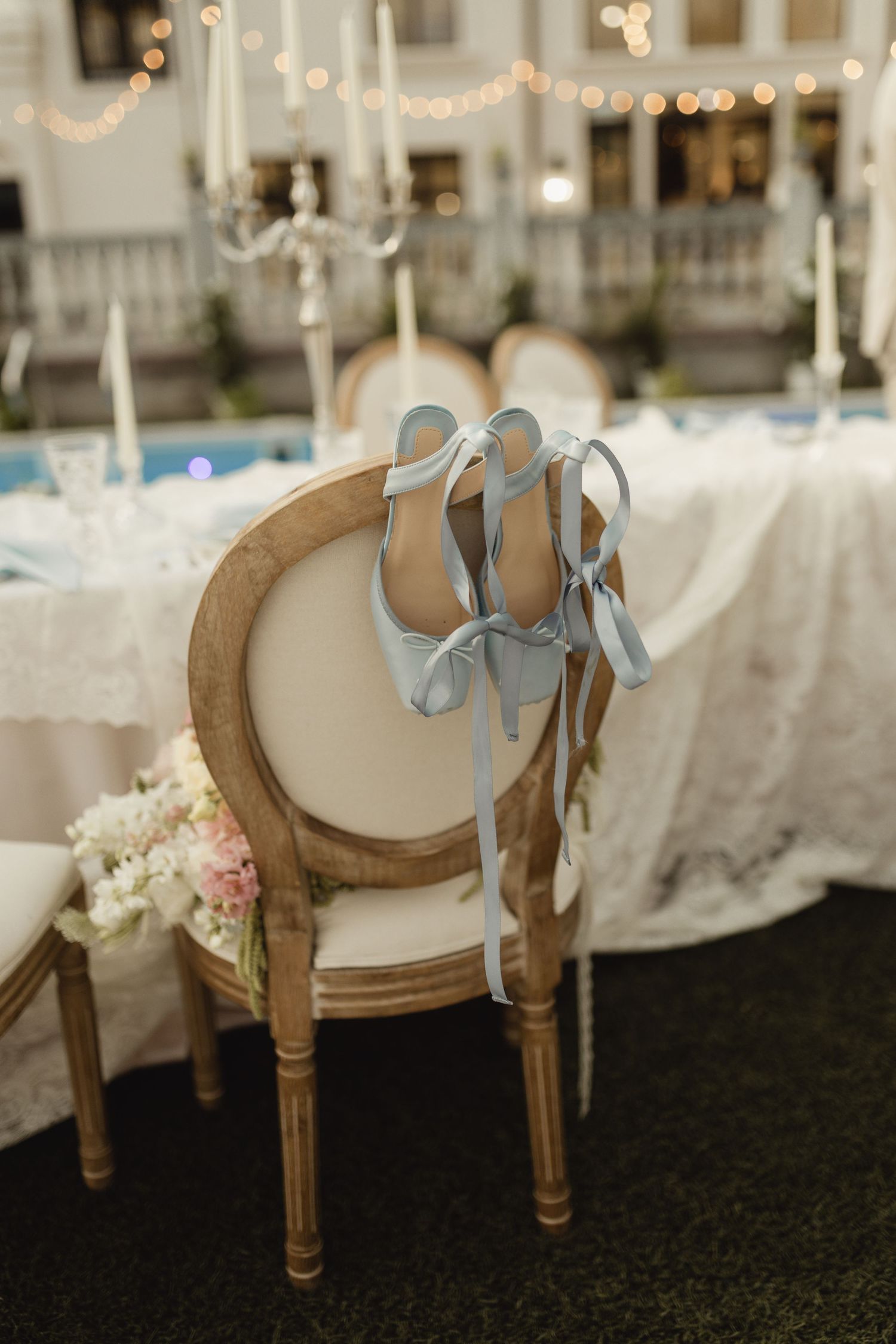 Light blue satin ribbon heels displayed on a wooden French Louis chair at an elegant wedding reception.