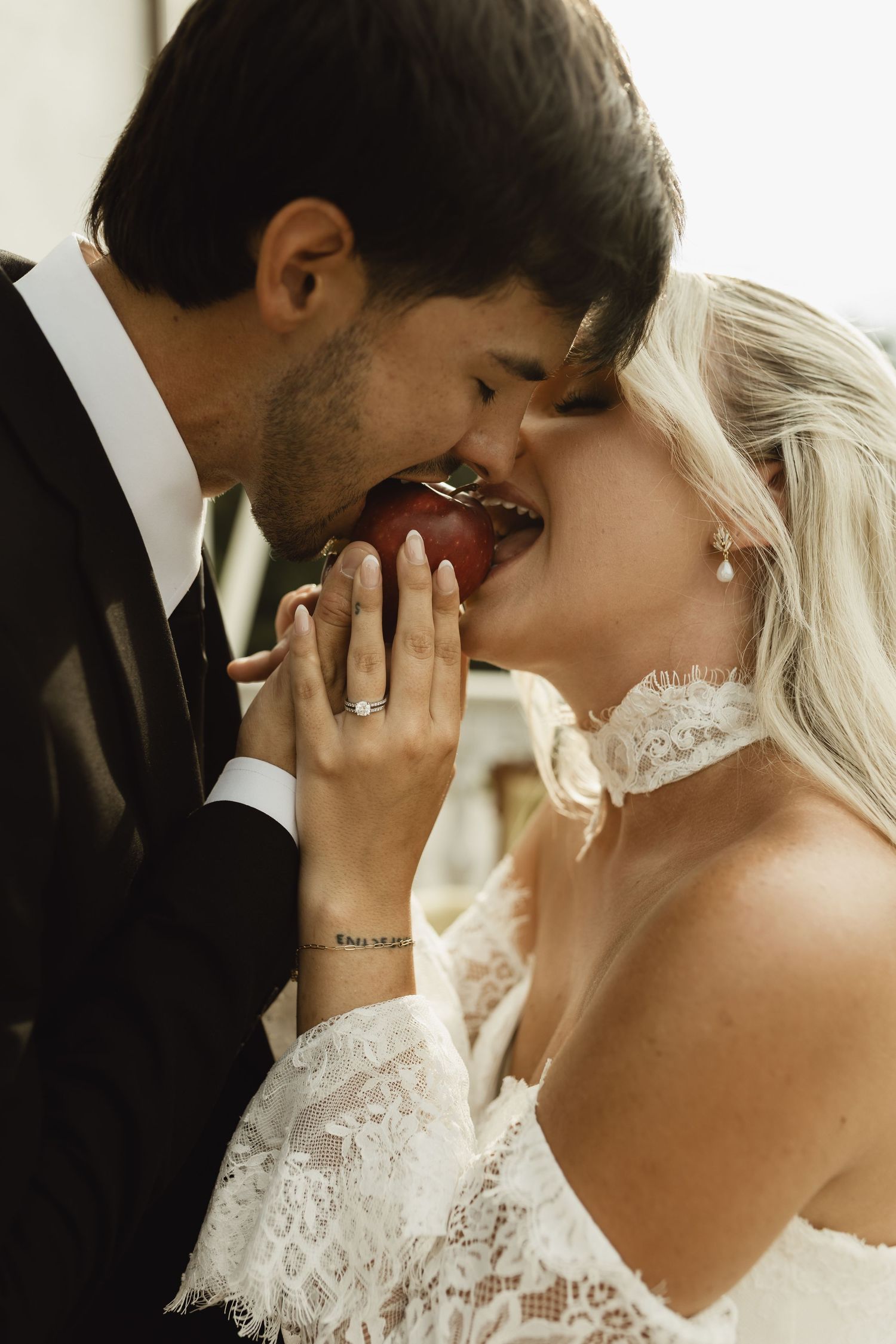 Bride and groom sharing a romantic apple bite together, bride wearing lace wedding dress and diamond engagement ring.