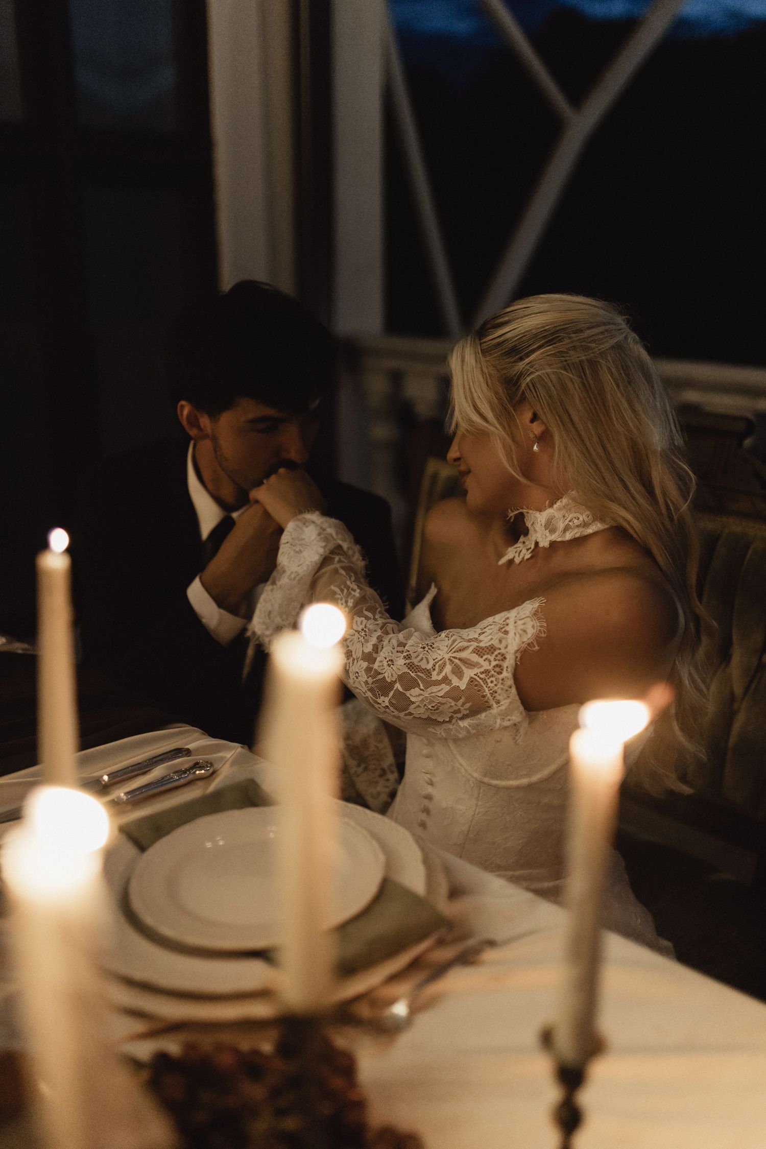 Bride and groom share a romantic candlelit dinner at their wedding reception table, glowing candles in the foreground.