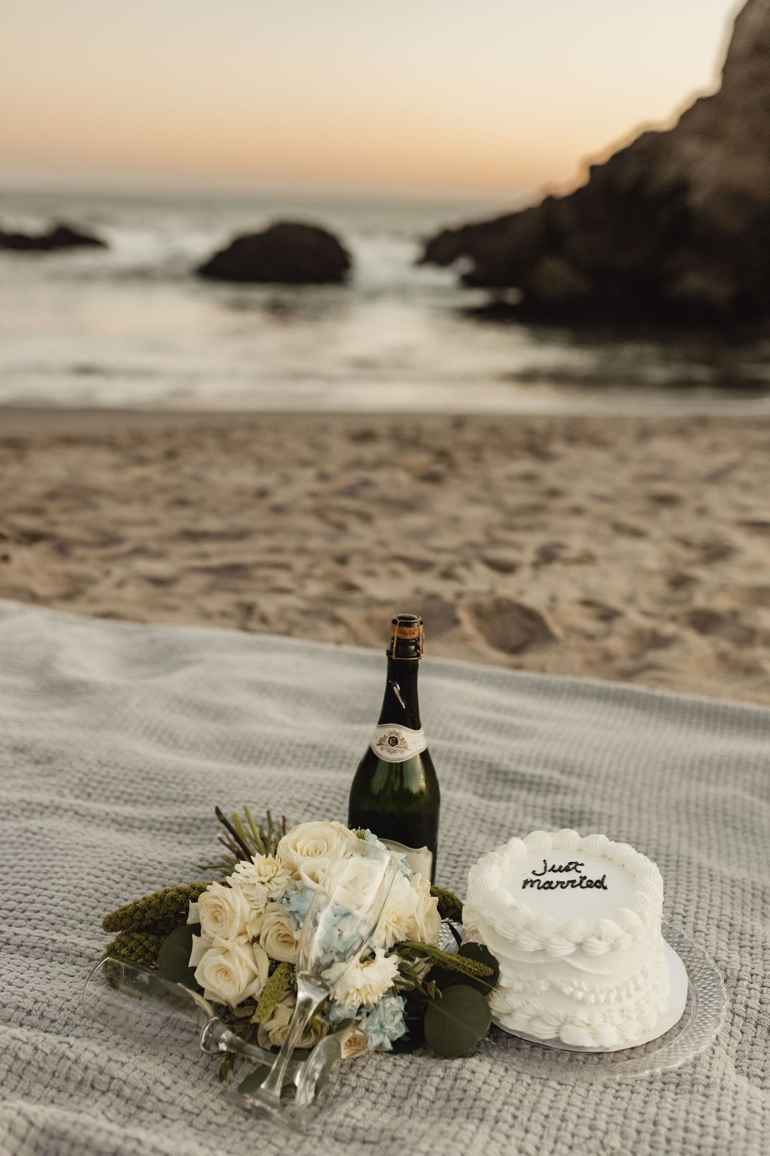 Wedding cake and champagne set up for a romantic beach picnic at sunset.