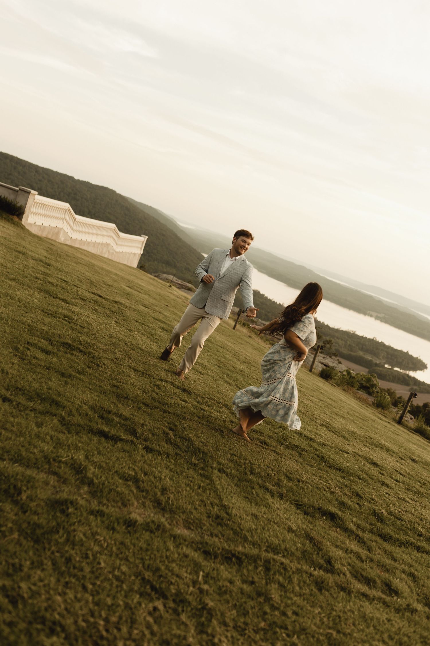 Couple playfully posing on a hilltop with scenic mountain views in the background.