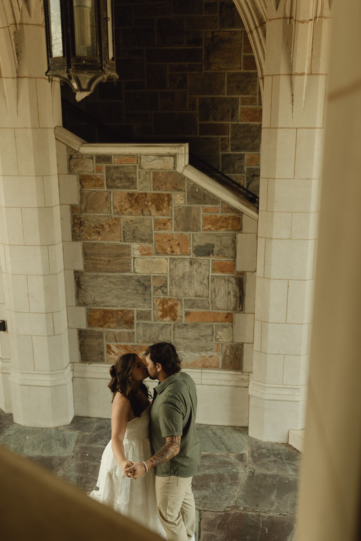 Bride and groom sharing an intimate kiss beneath stone arches of an elegant historic wedding venue.