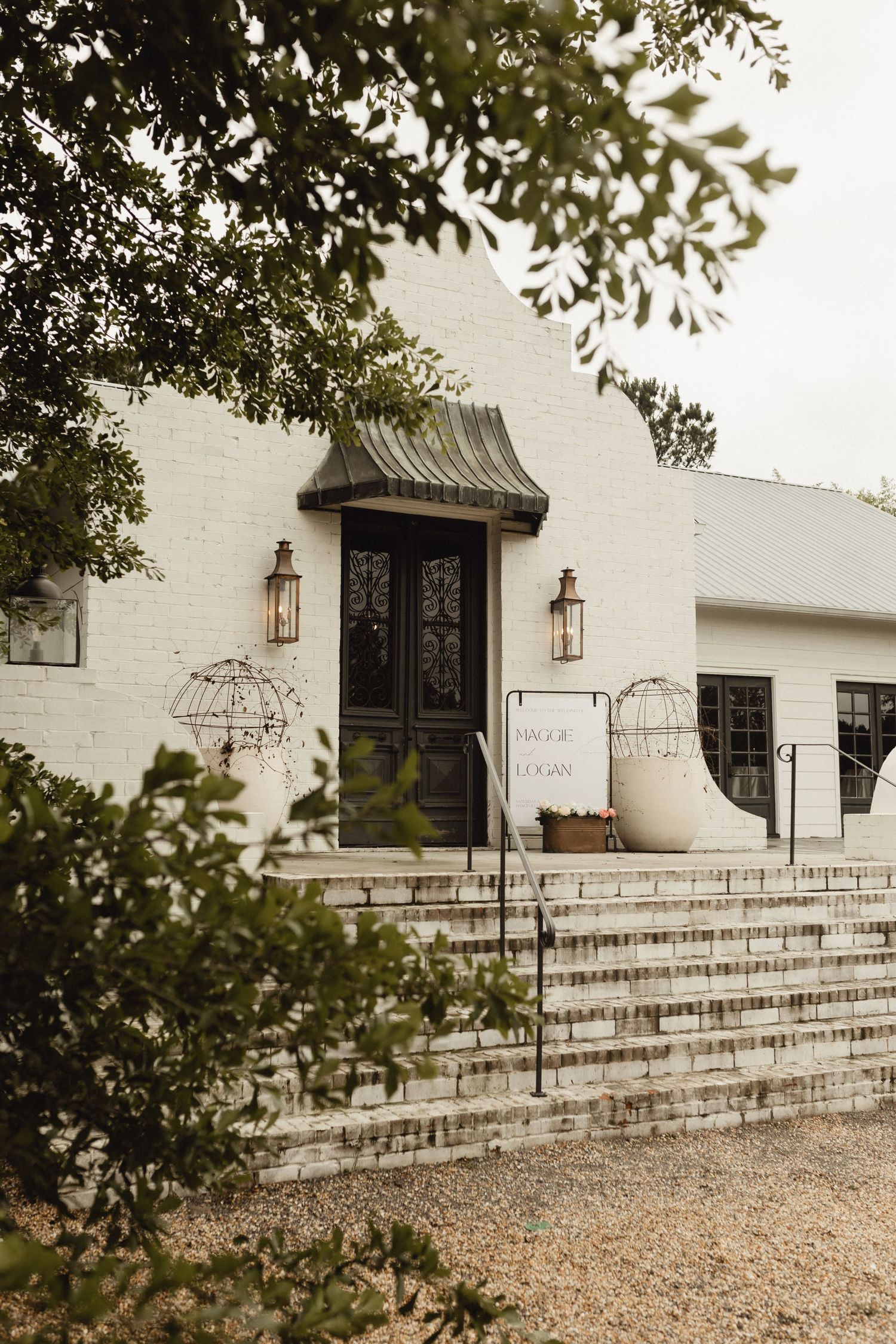 White stone church entrance with rustic lanterns and gravel pathway leading to wooden double doors.