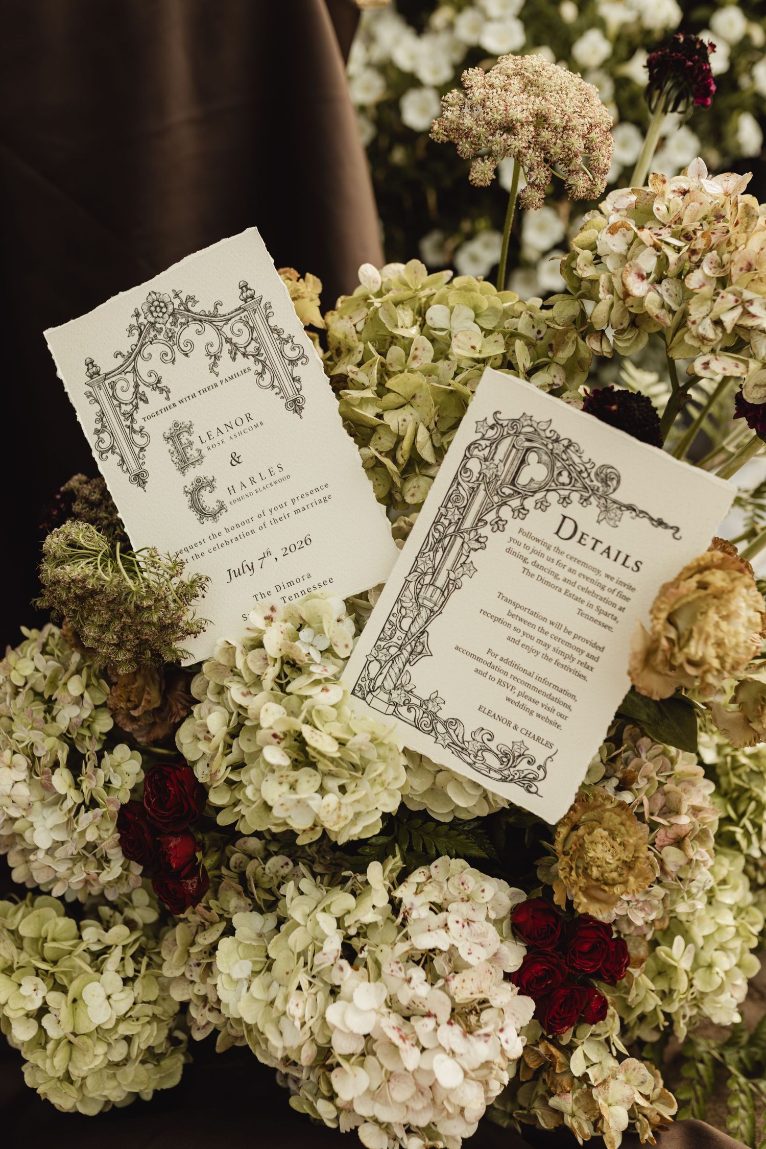 Elegant wedding stationery with ornate black borders resting on lush white and green hydrangeas with deep red accents.