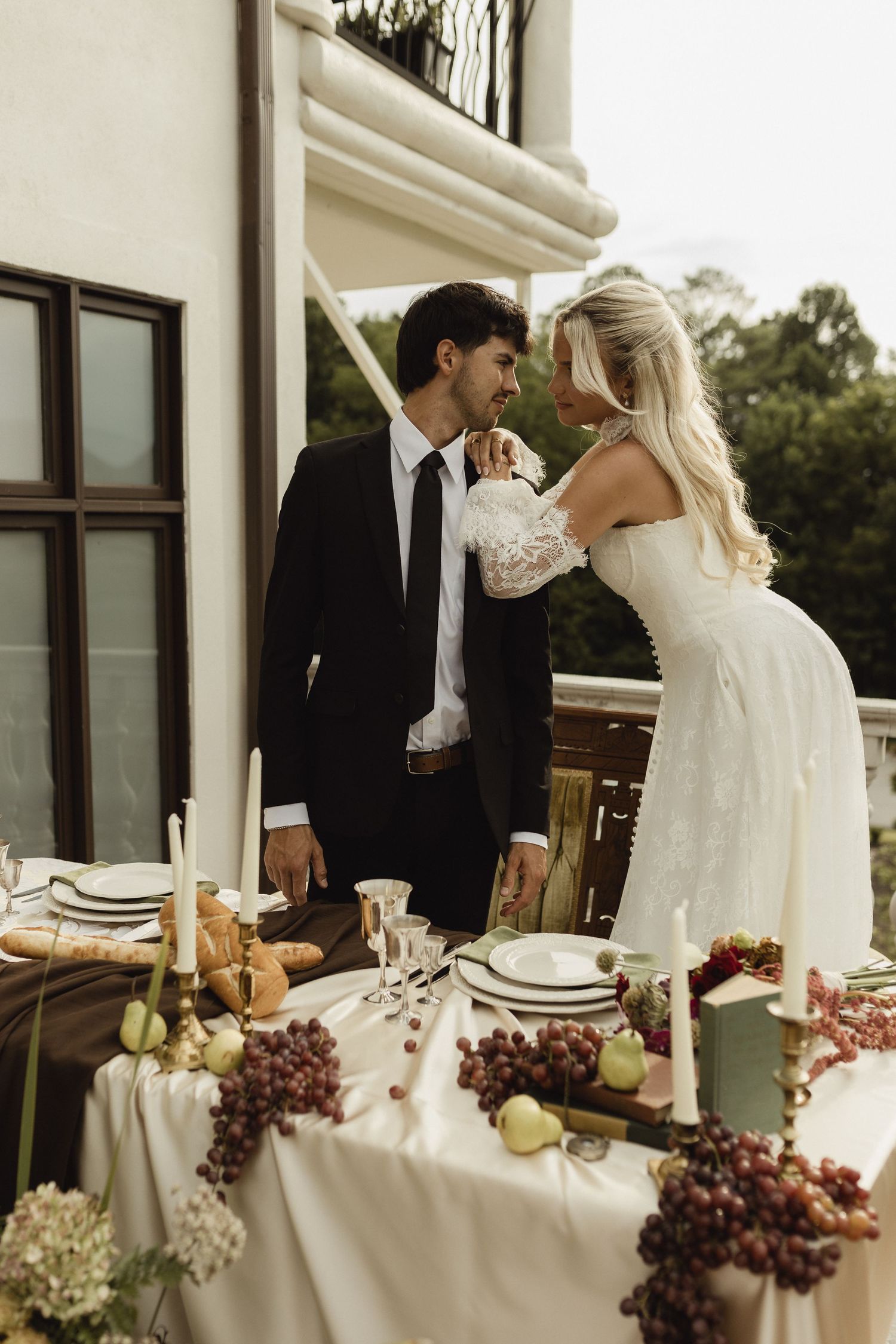 Bride and groom share an intimate moment at an elegantly decorated outdoor wedding reception table with fruit and candles.