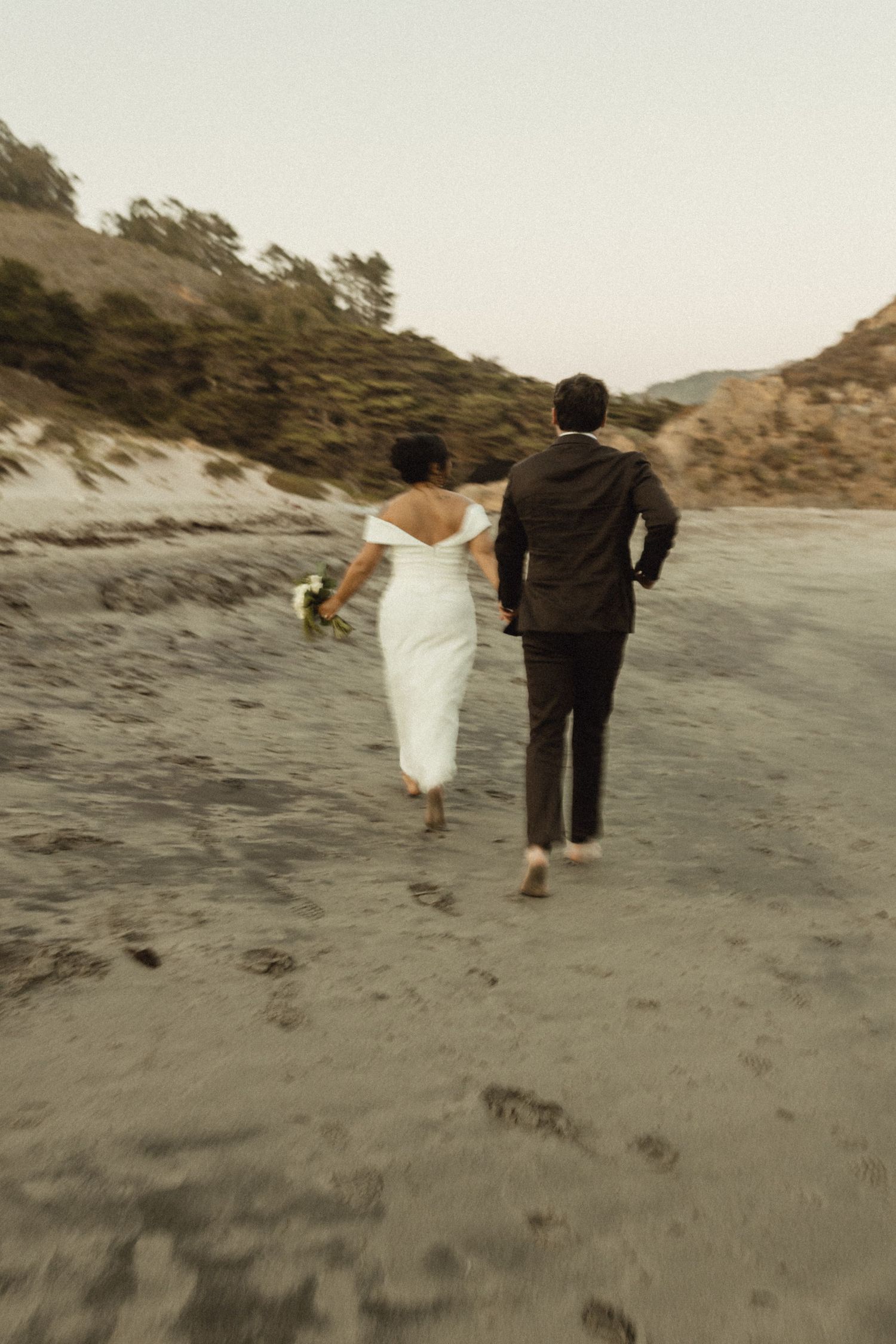A couple walks hand in hand along a misty coastal beach.
