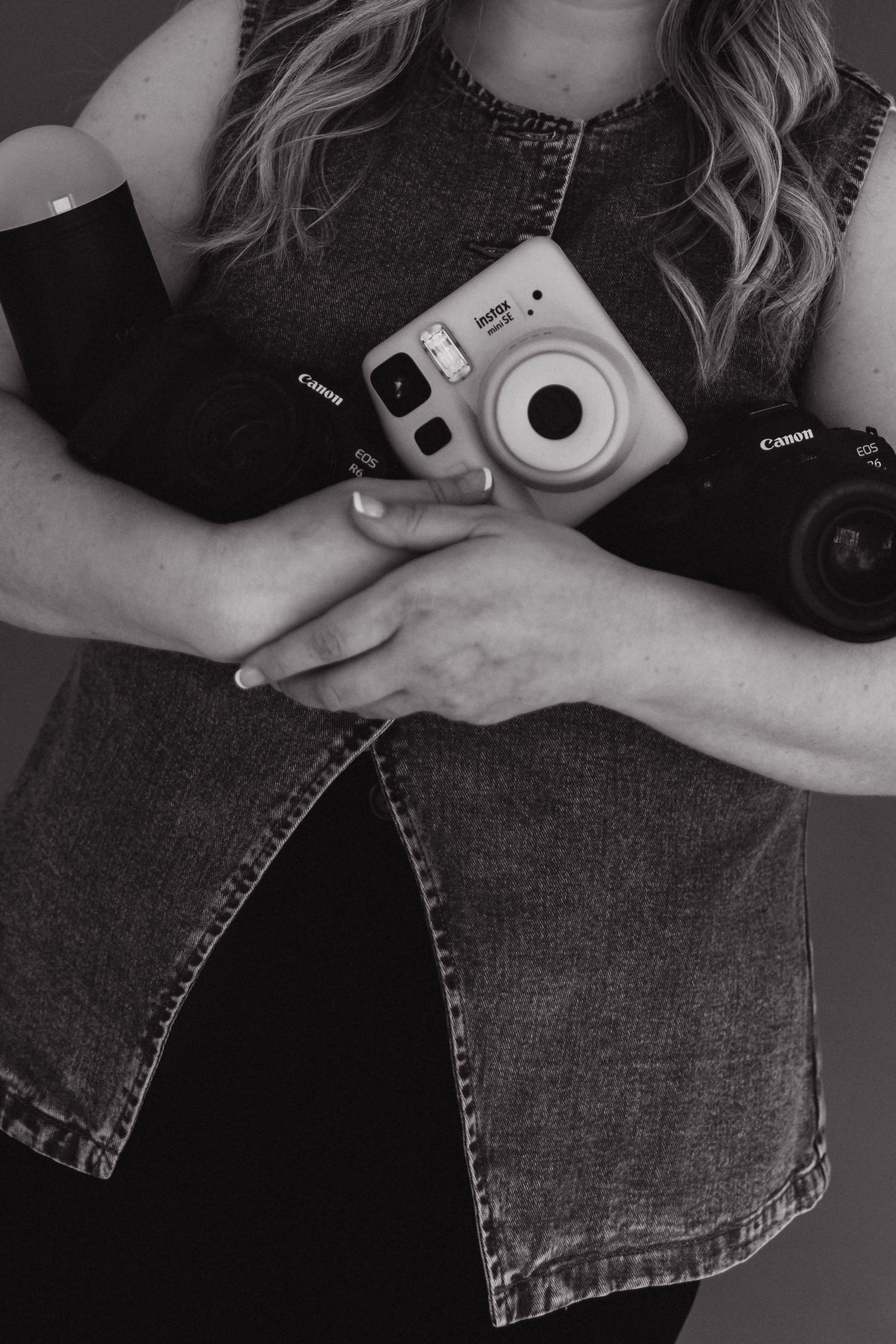 Black and white photo of a woman holding Canon cameras and a Fujifilm Instax Mini instant camera against her chest.