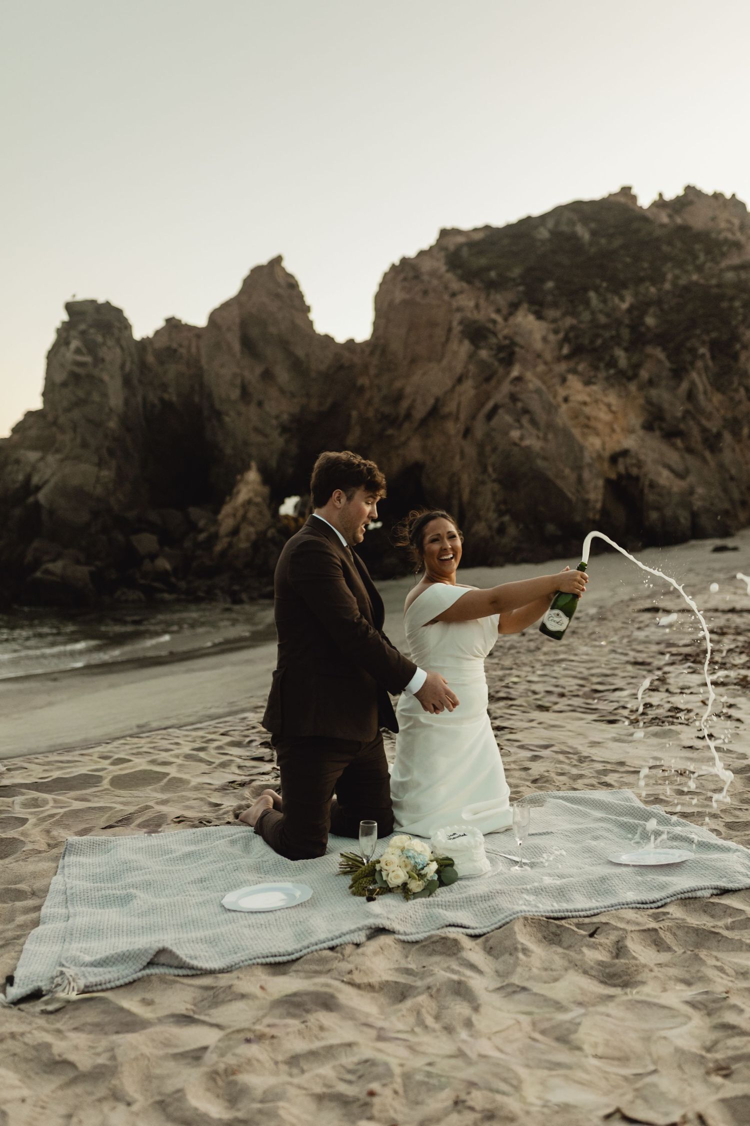 A romantic beach wedding photoshoot with rocky cliffs and waves in the background.