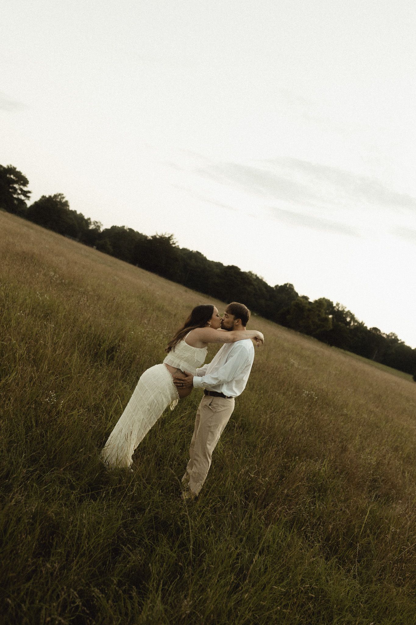Romantic couple sharing a kiss in a lush green meadow during golden hour wedding photo session.
