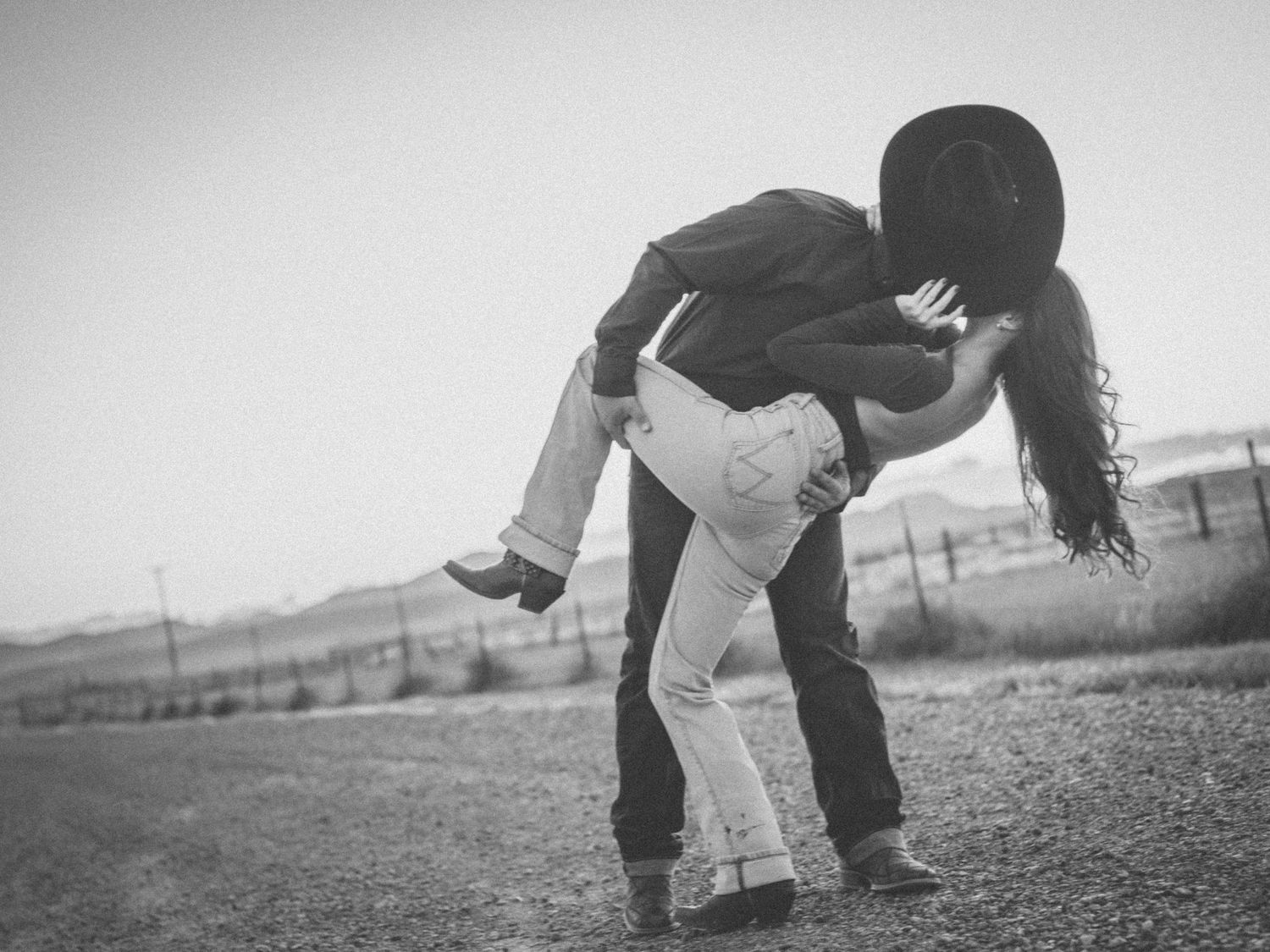 A playful black and white photo of a couple dancing in a field.