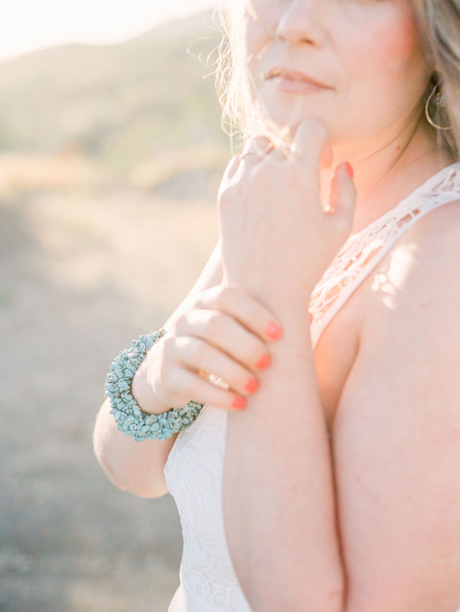 Delicate turquoise bracelet adorns a bride's wrist in soft sunlit glow.