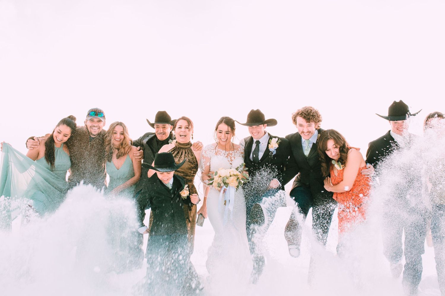 A joyful wedding party runs through a cloud of smoke or mist during an outdoor celebration.