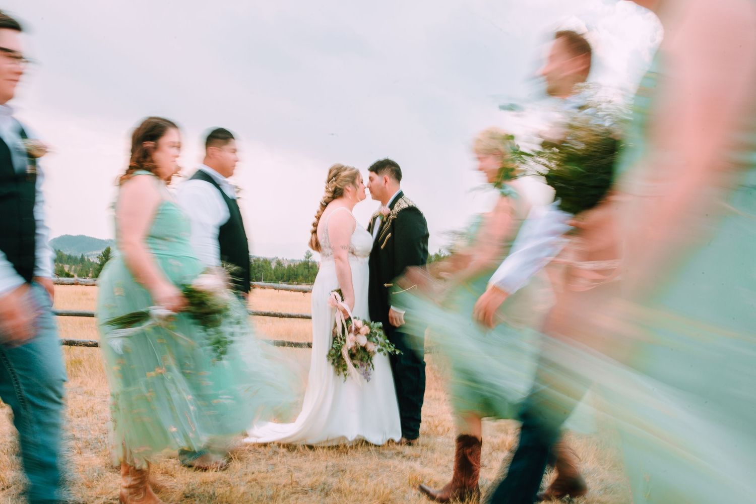 A wedding couple and guests dance in a blurred motion sequence on an outdoor patio at sunset.
