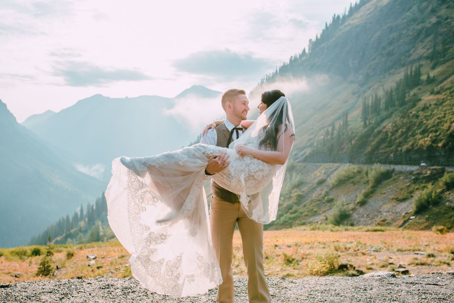 A couple embraces during their mountain wedding photoshoot with dramatic peaks and golden light in the background.