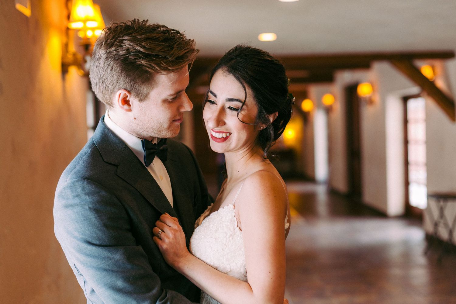 A couple shares a tender moment in an elegant indoor venue with warm lighting and rustic wooden beams.