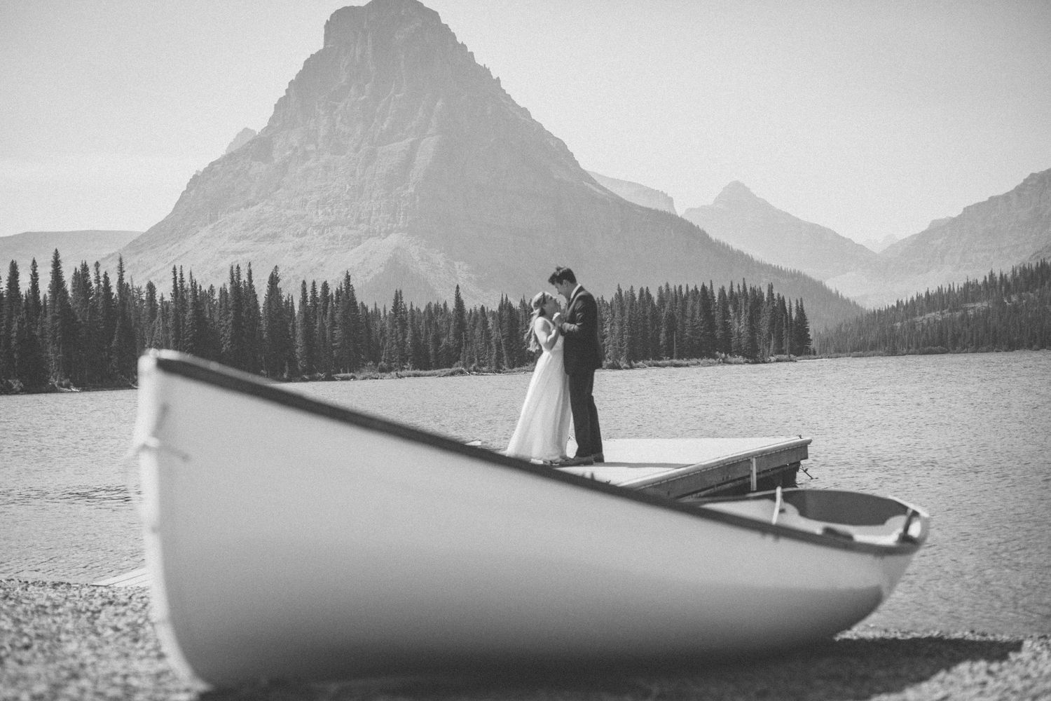 Black and white photo of boats moored on a mountain lake with dramatic peaks rising in the misty background.