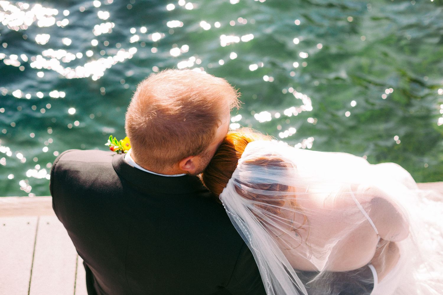 Newlyweds share an intimate moment by sparkling water on a sunny day.
