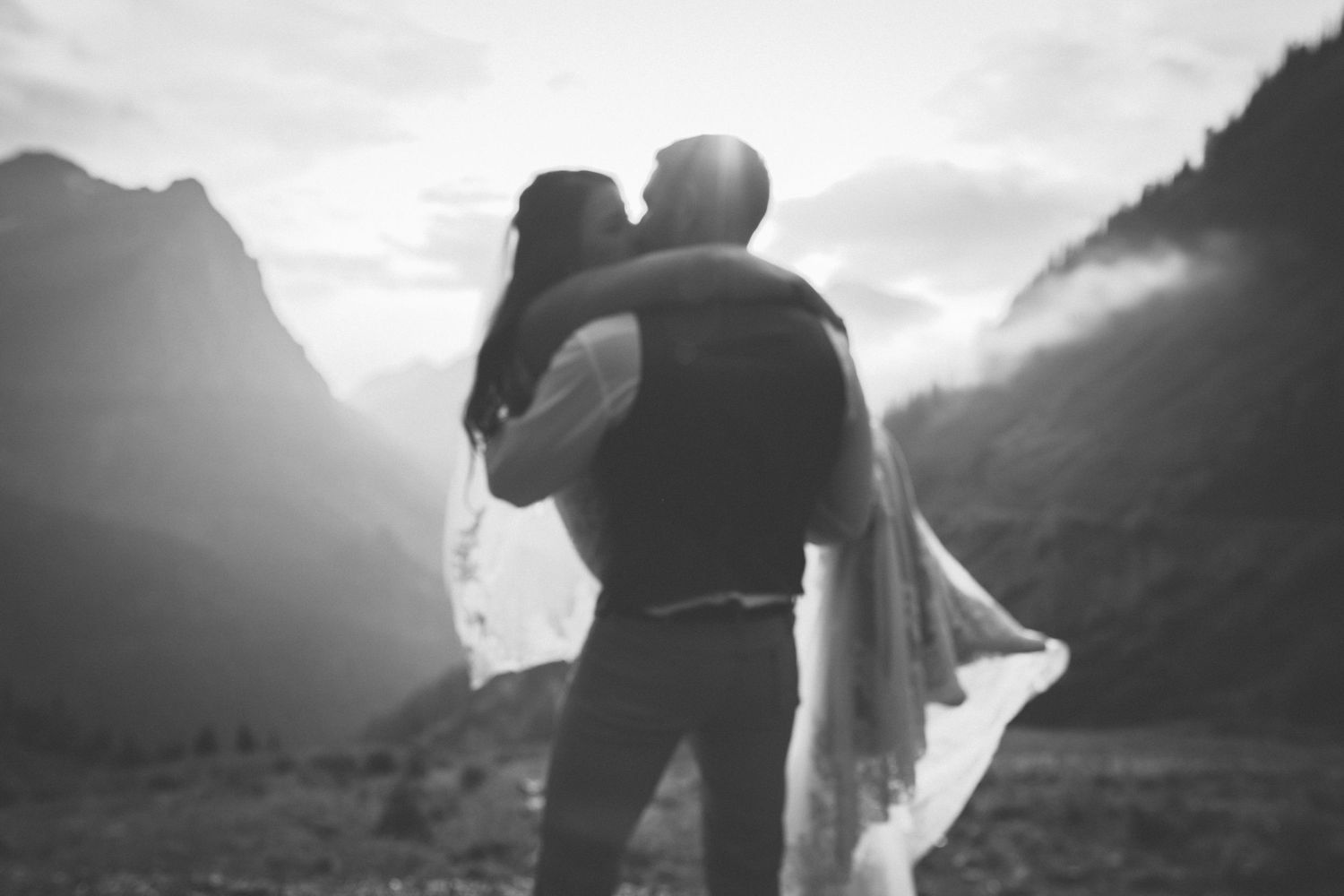 Black and white romantic wedding photos showing silhouettes of a couple embracing against dramatic mountain landscapes.