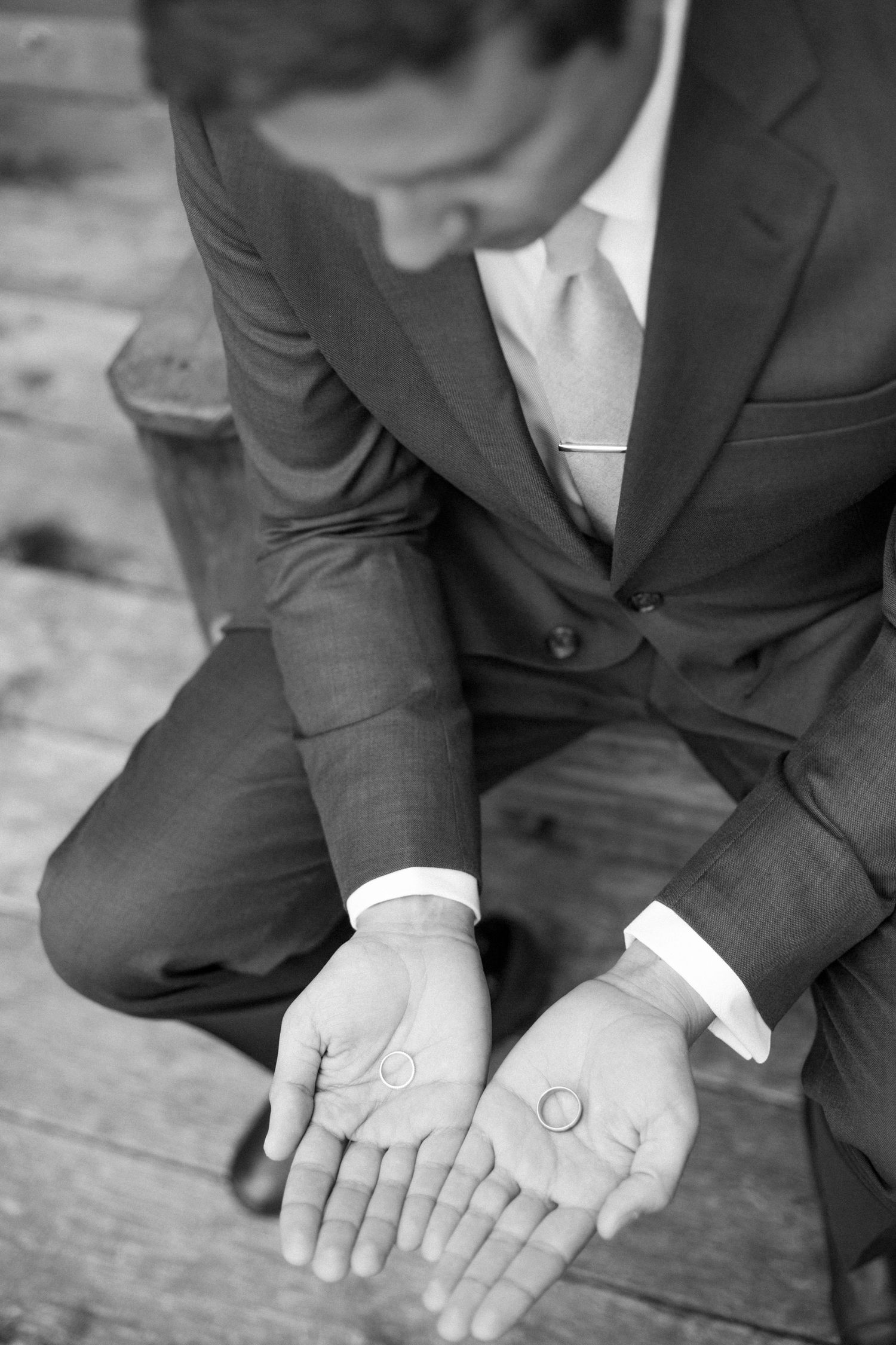 Close-up of wedding rings held in open palms wearing formal suit attire.