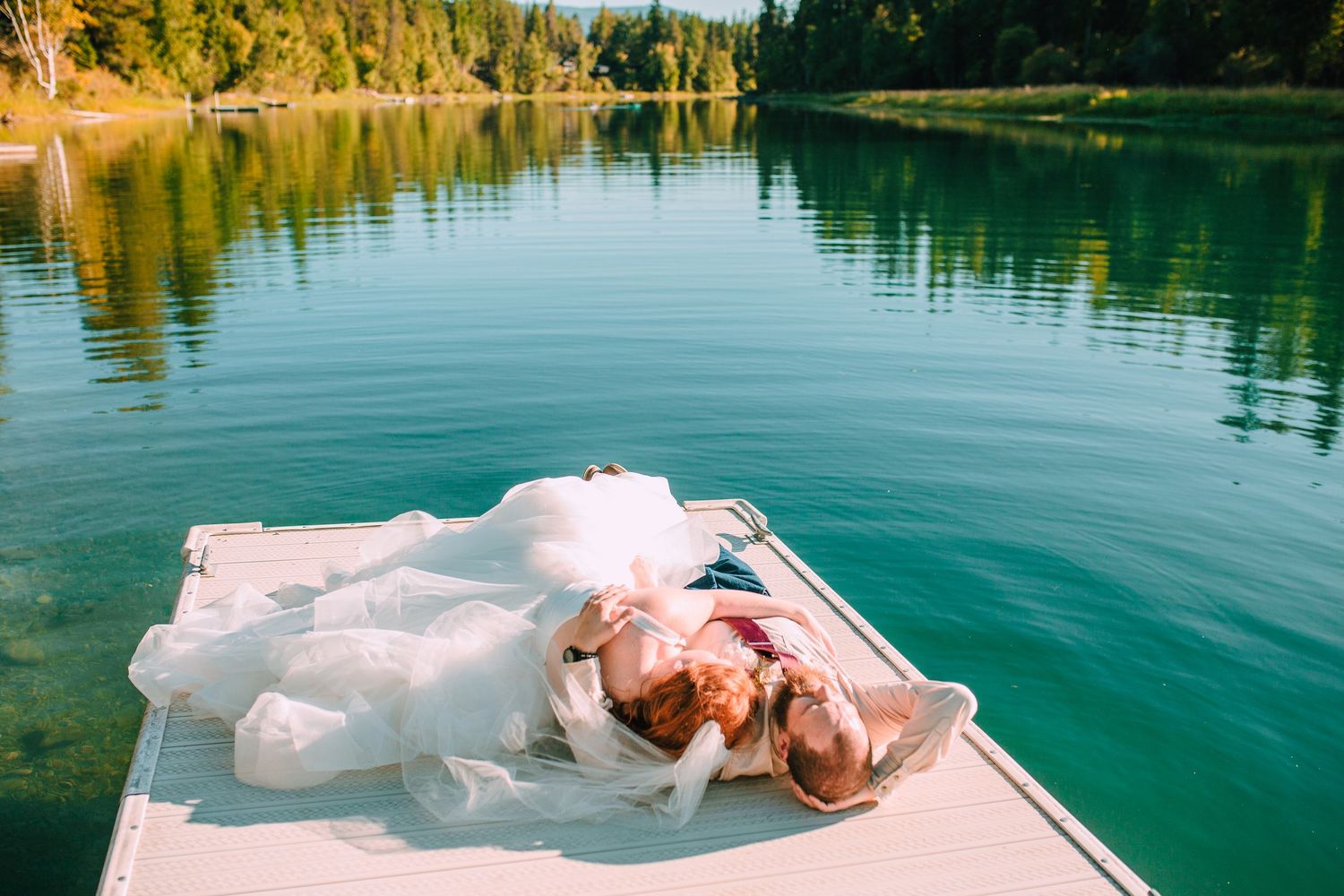 A couple in wedding attire relaxing on a boat deck surrounded by pristine lake waters.