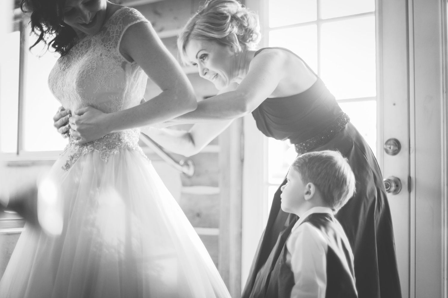 Black and white photos of a bride's mother helping her into her wedding dress, while her son watches.