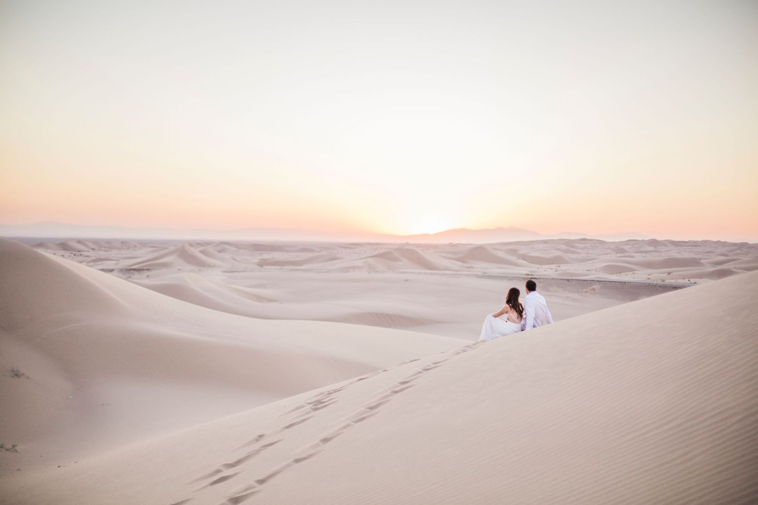 Couple creates footprints while walking through vast desert landscape at sunset.