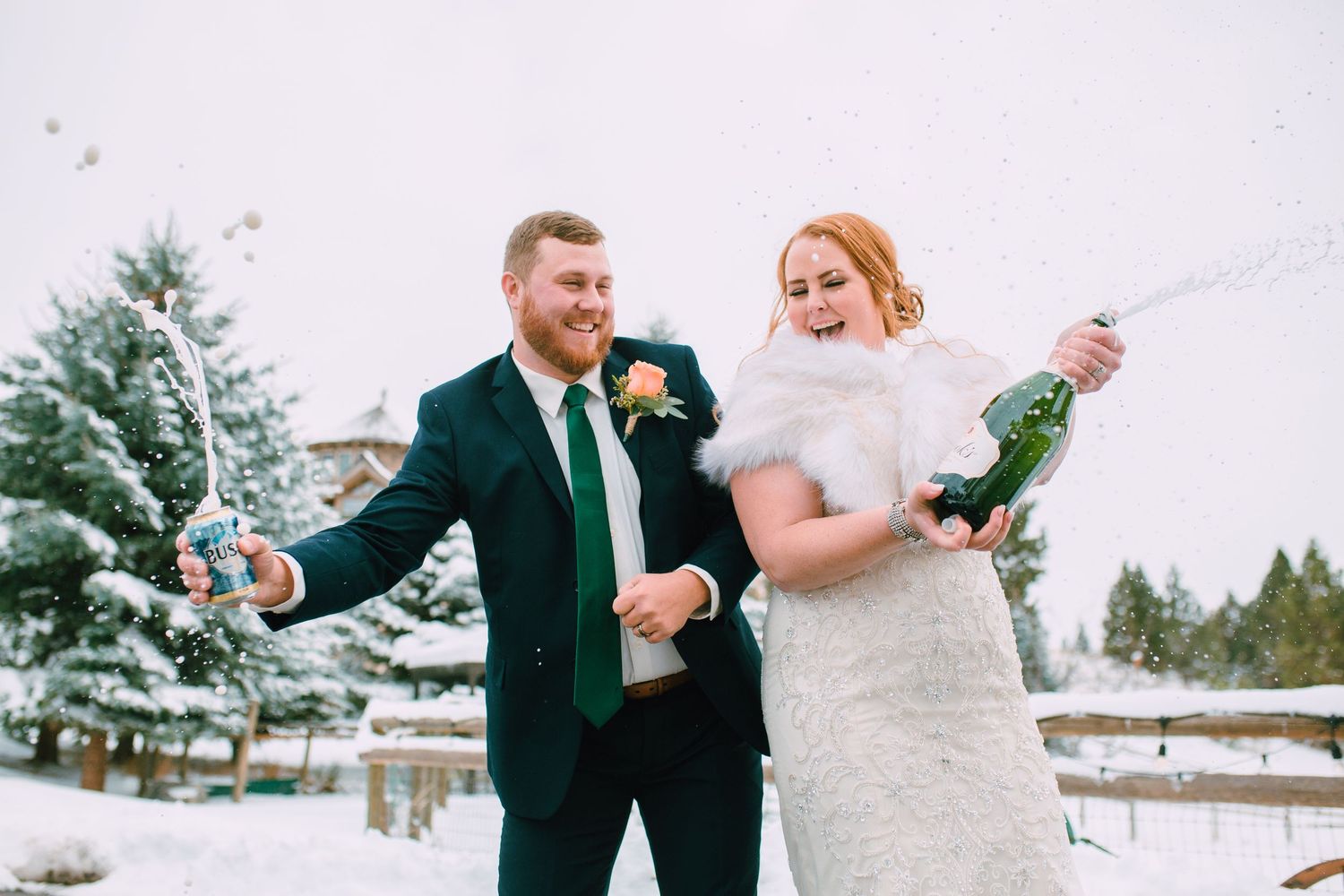 A bride and groom celebrate with champagne in a snowy winter setting wearing formal wedding attire.