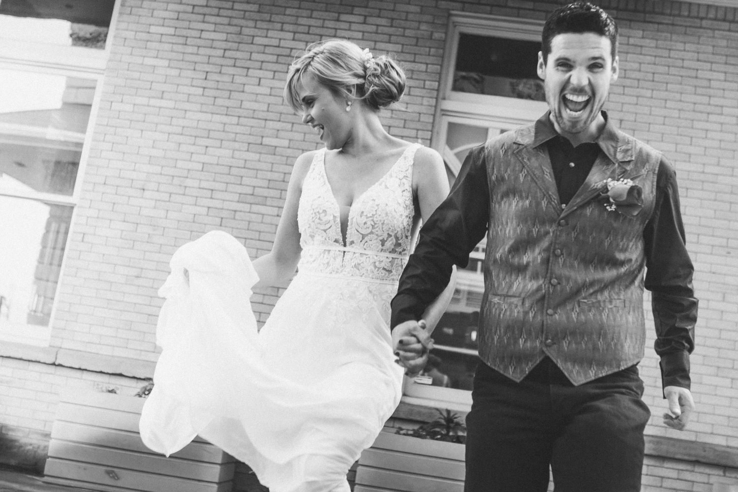 A wedding couple dances and laughs together on a brick-lined pathway.