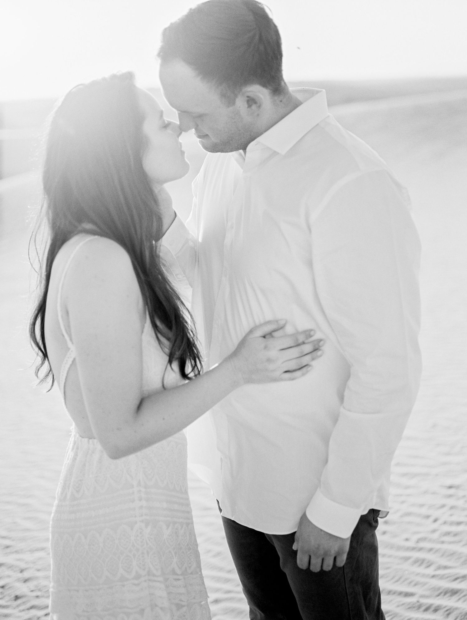 Intimate couple shares tender moment against bright desert backdrop.