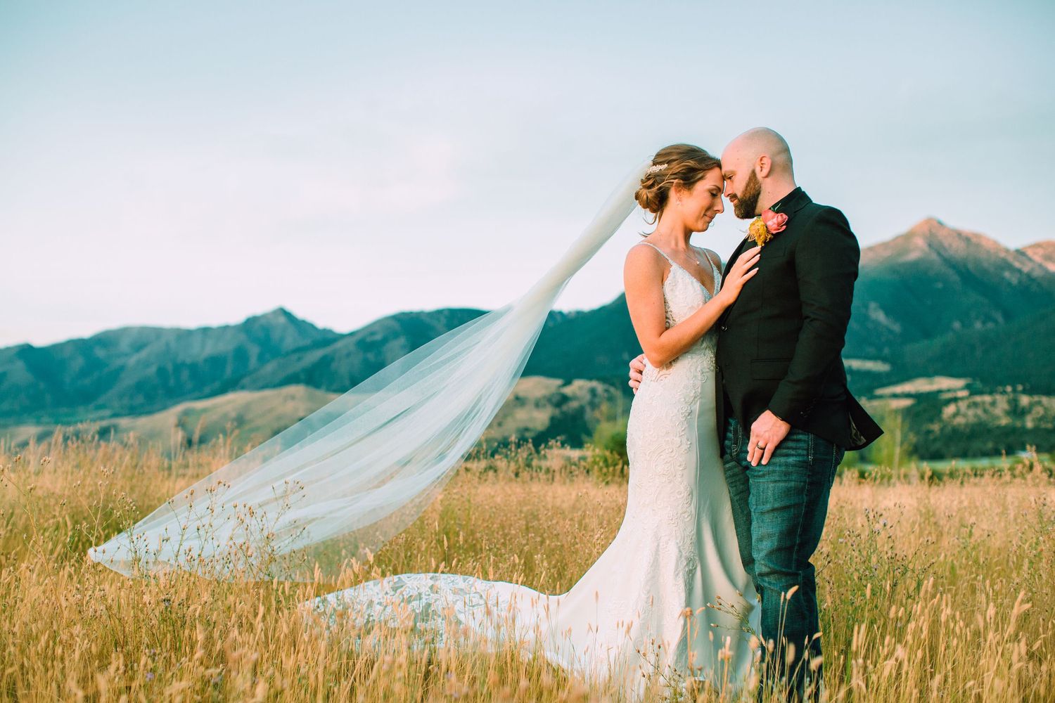 A couple shares a romantic moment in a mountain meadow with a flowing white veil caught in the breeze.