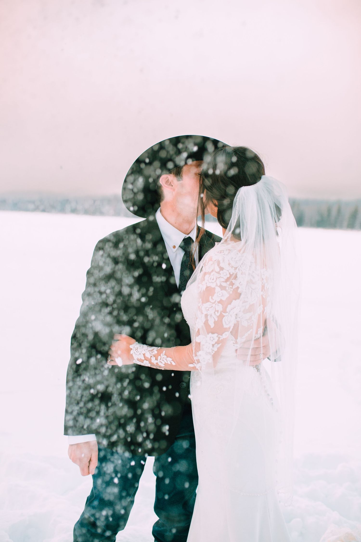 A romantic winter wedding photo with snow falling around the couple in formal attire.