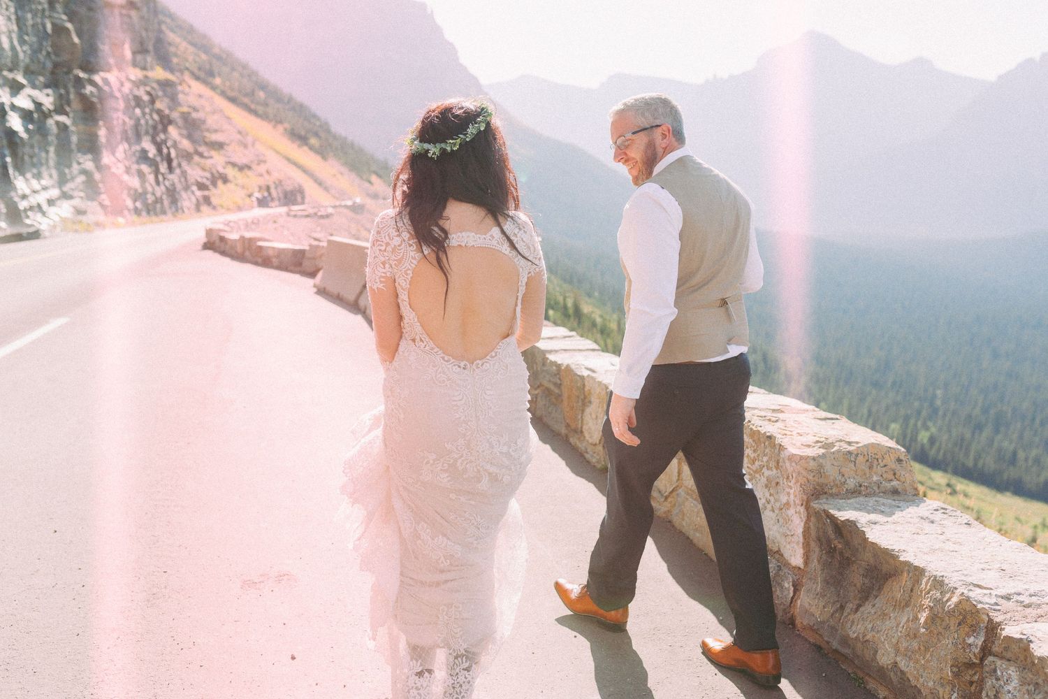 A couple in wedding attire poses on a scenic mountain overlook with dramatic mountain vistas in the background.