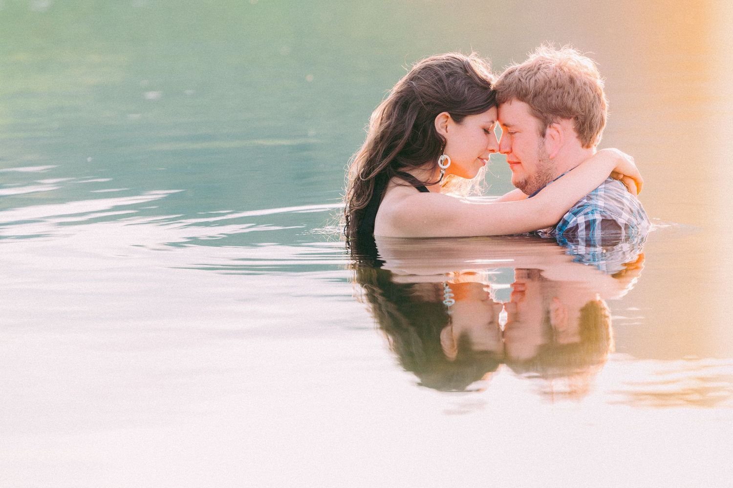 A couple shares a romantic kiss while floating in turquoise water during a Montana photo session.