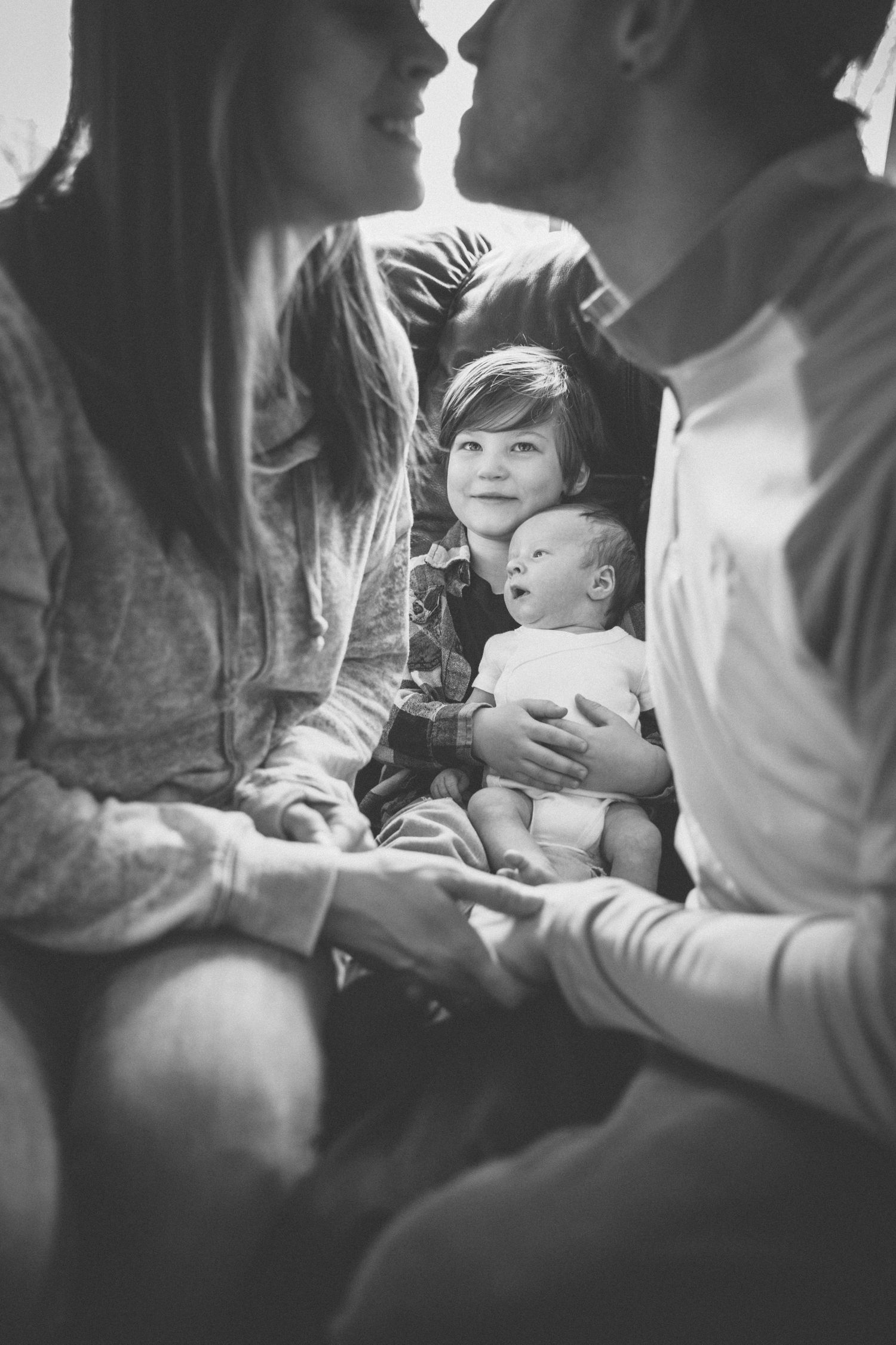 A series of black and white photos showing tender moments between parents and their baby in intimate home settings.