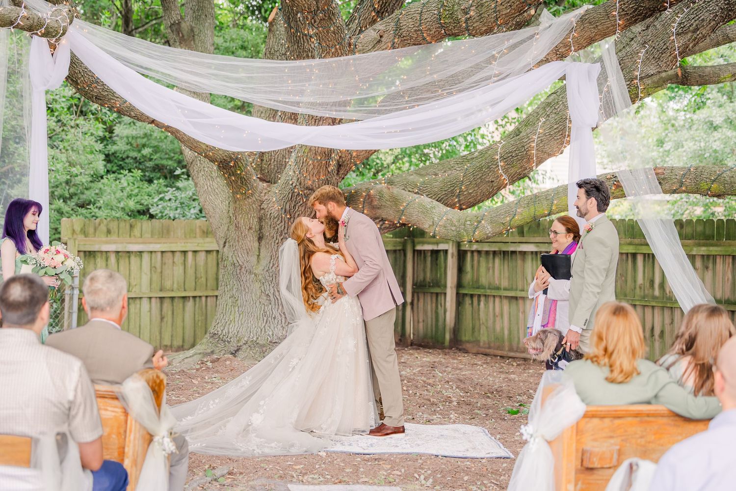 Wedding ceremony moment under draped fabric and tree branches with seated guests looking on in a backyard wedding in wilmington, nc