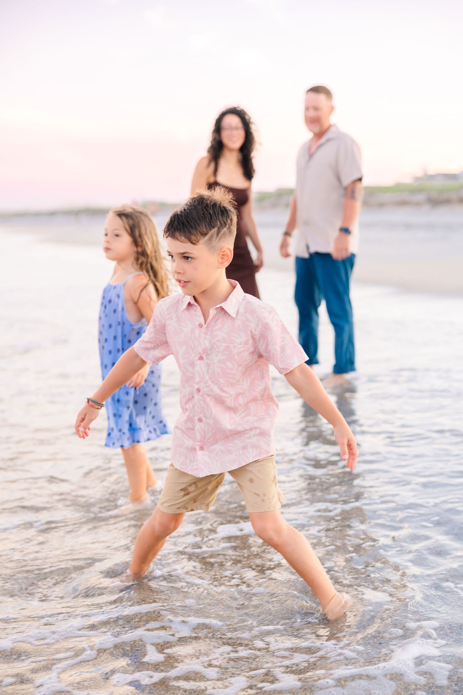Family of four enjoying sunset walk in ocean waves at beach.