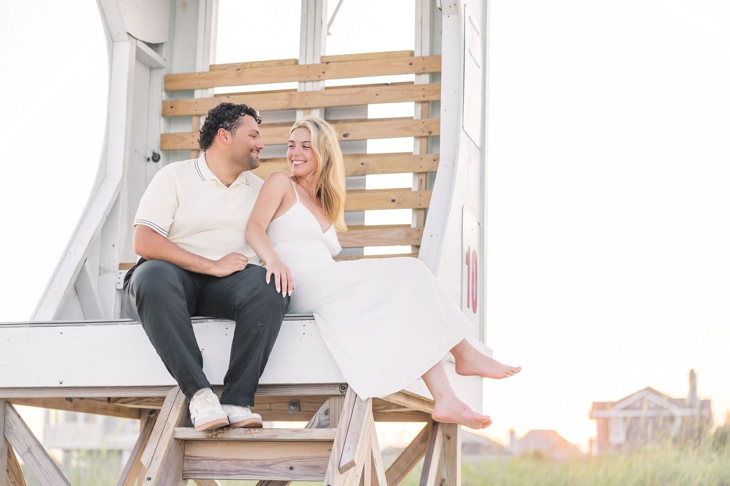 Happy couple sits atop a wooden lifeguard stand sharing a laugh at the beach.