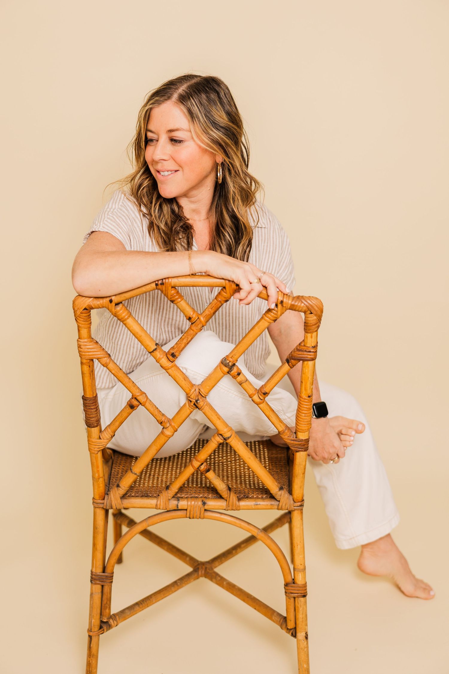Person poses playfully with bamboo chair against neutral studio backdrop.