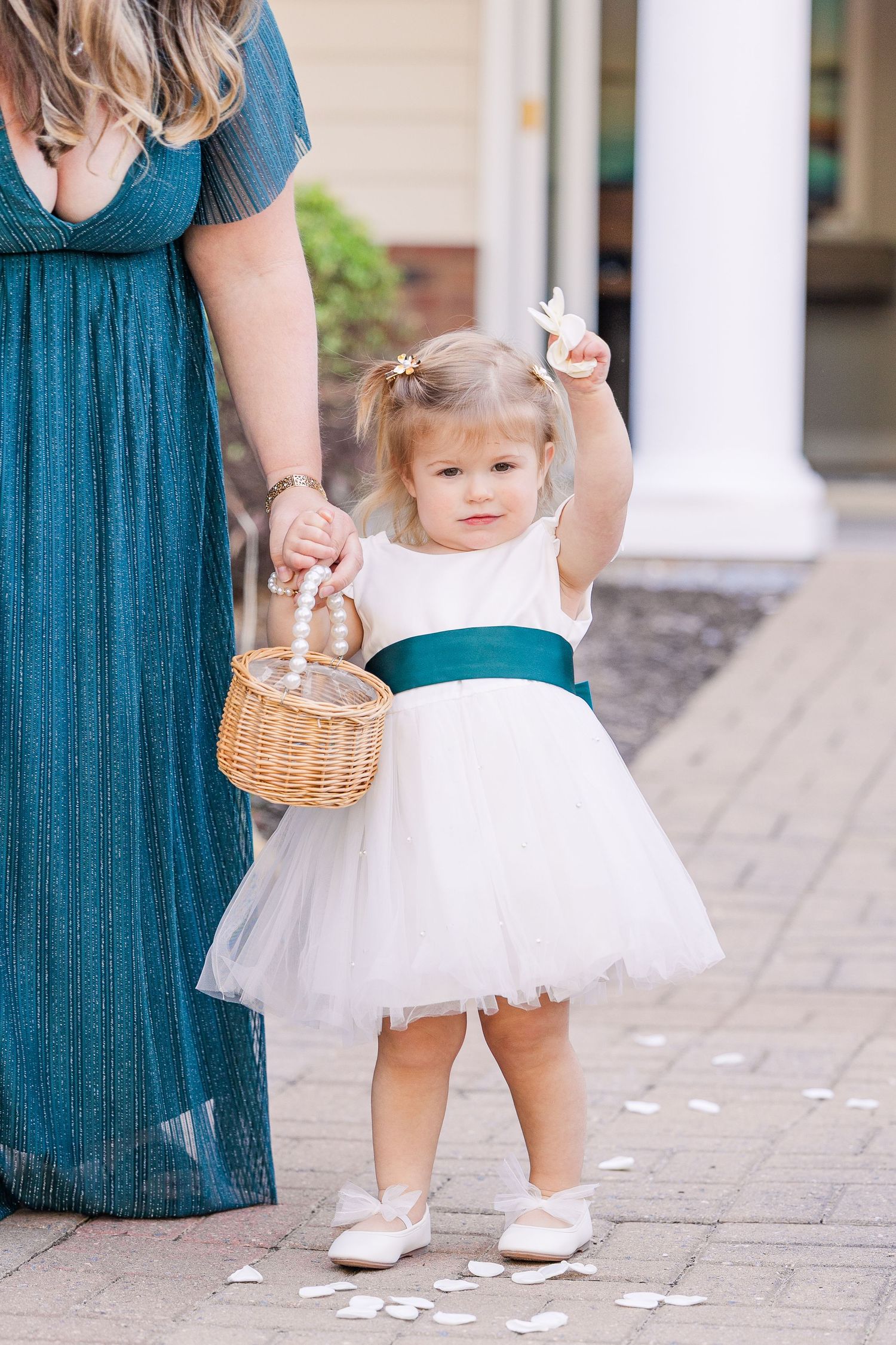 Small flower girl in white dress holding basket walks on stone path with scattered petals wedding groom bride lake Gaston photographer light