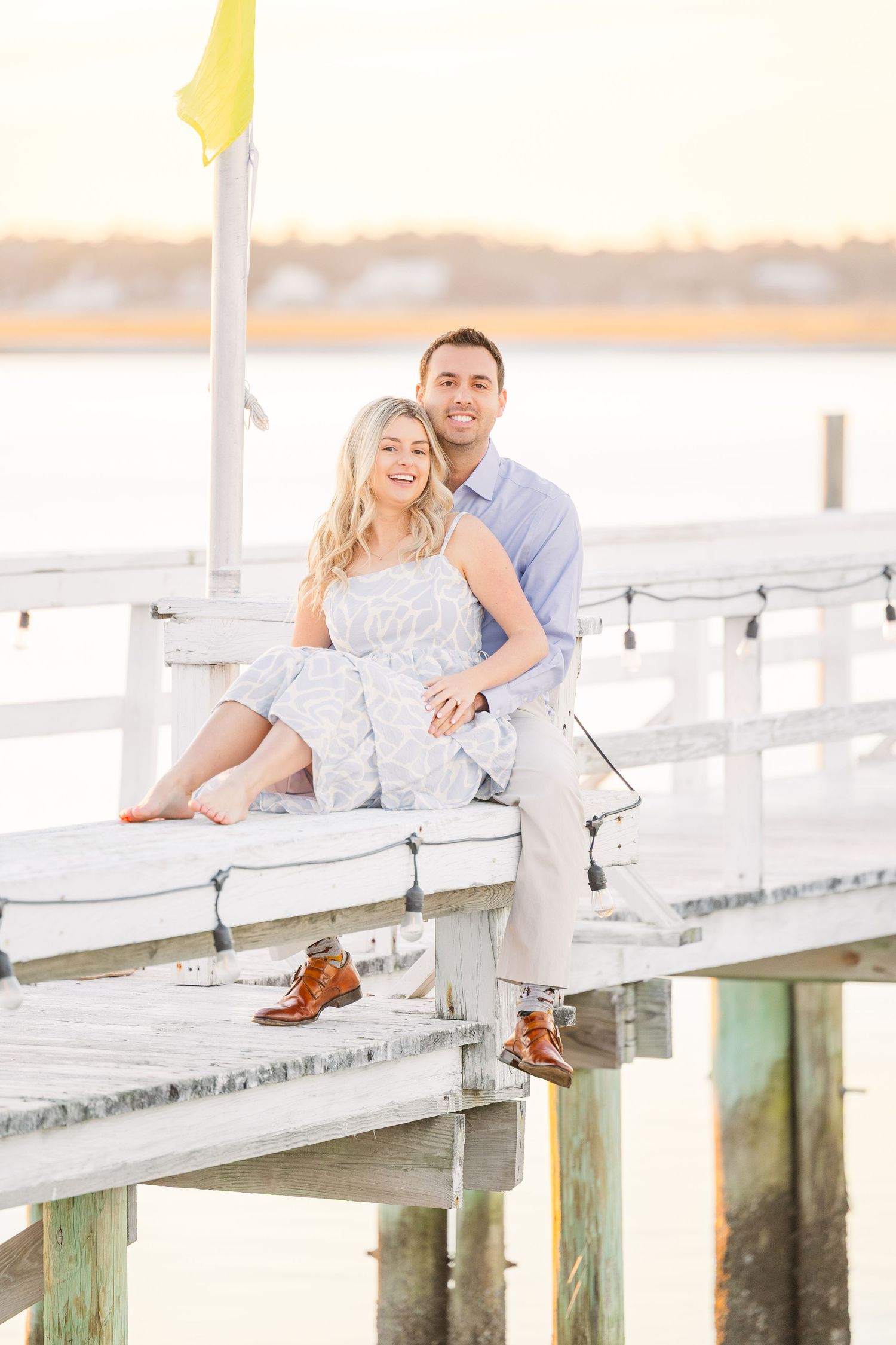 Couple sitting casually on white dock railing with water and sunset views.