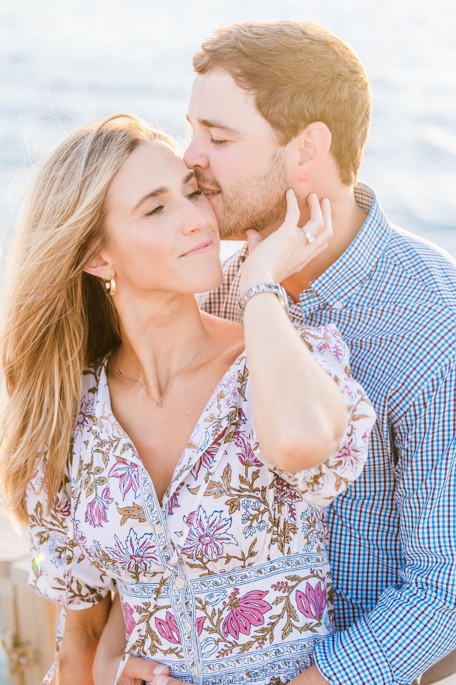 A romantic close-up moment between a couple against a soft coastal background.