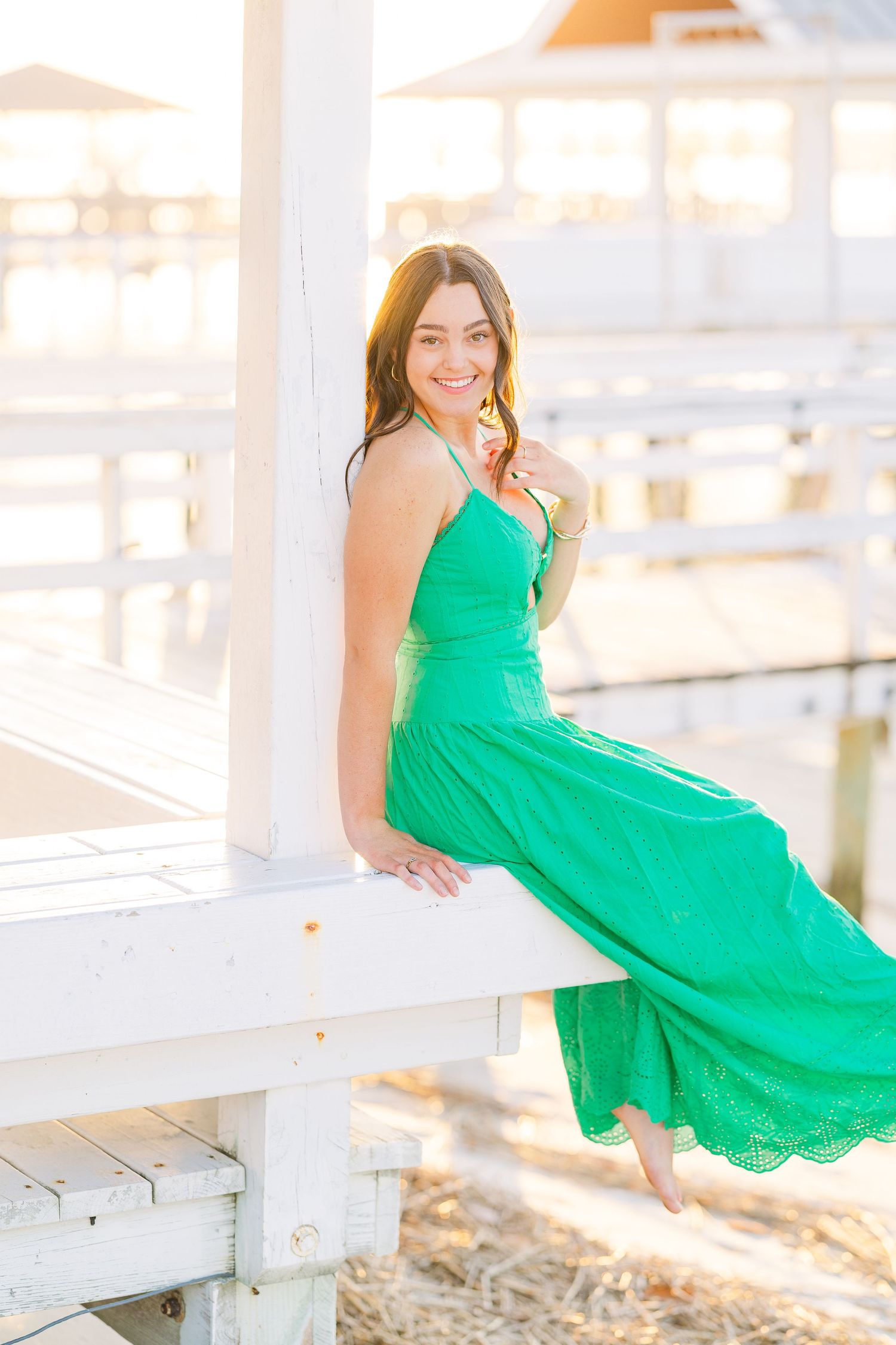 An emerald green maxi dress flows elegantly on a white coastal dock at sunset.